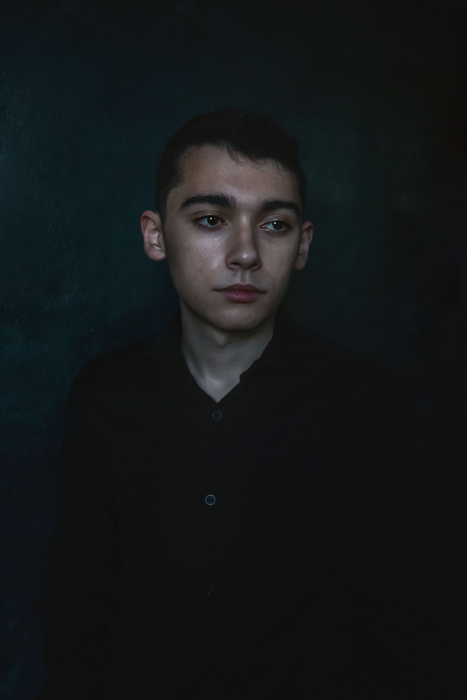 Moody low-key portrait showing person in dark clothing against dramatic shadowed background.