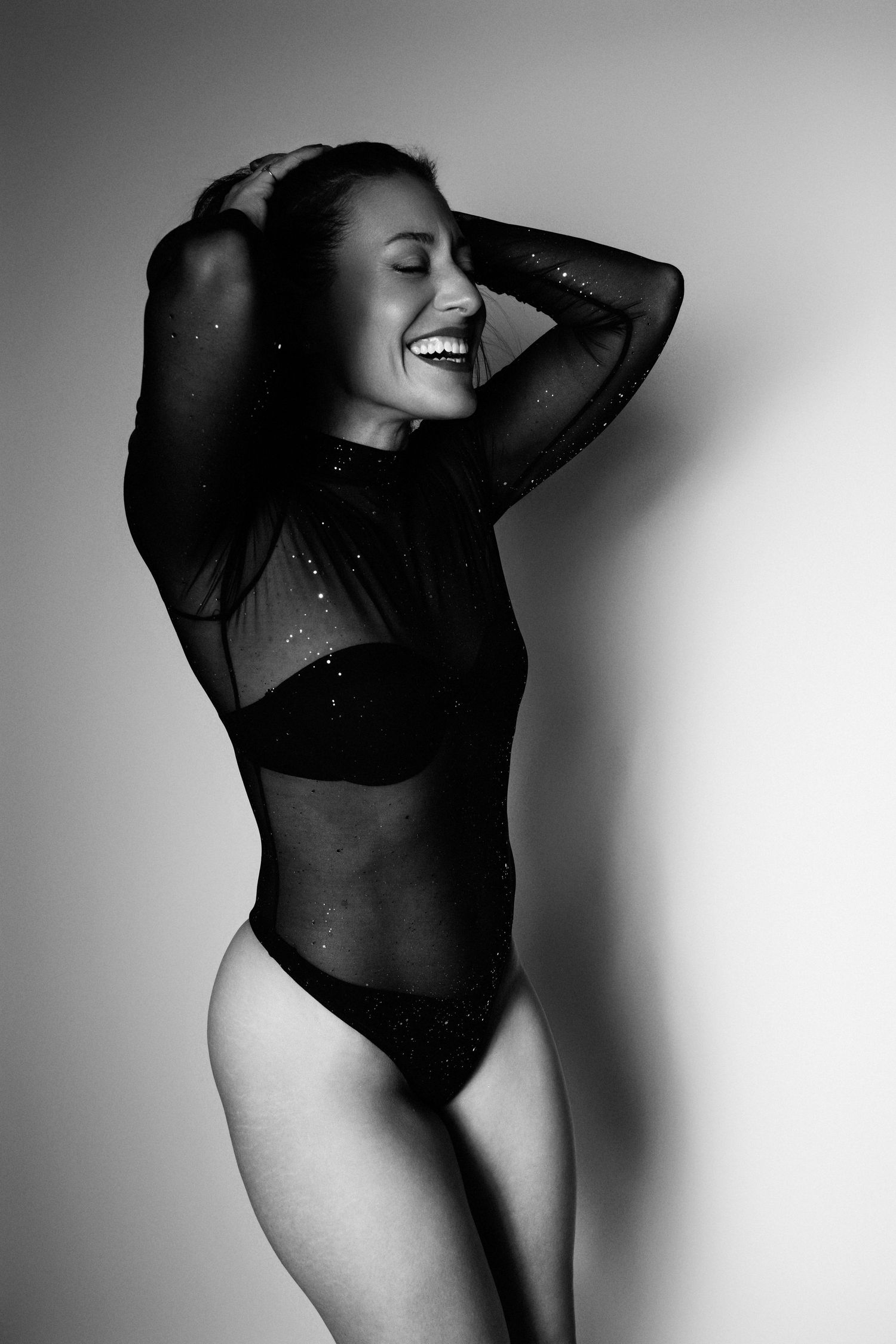 Black and white artistic photo of a model posing in sheer bodysuit.