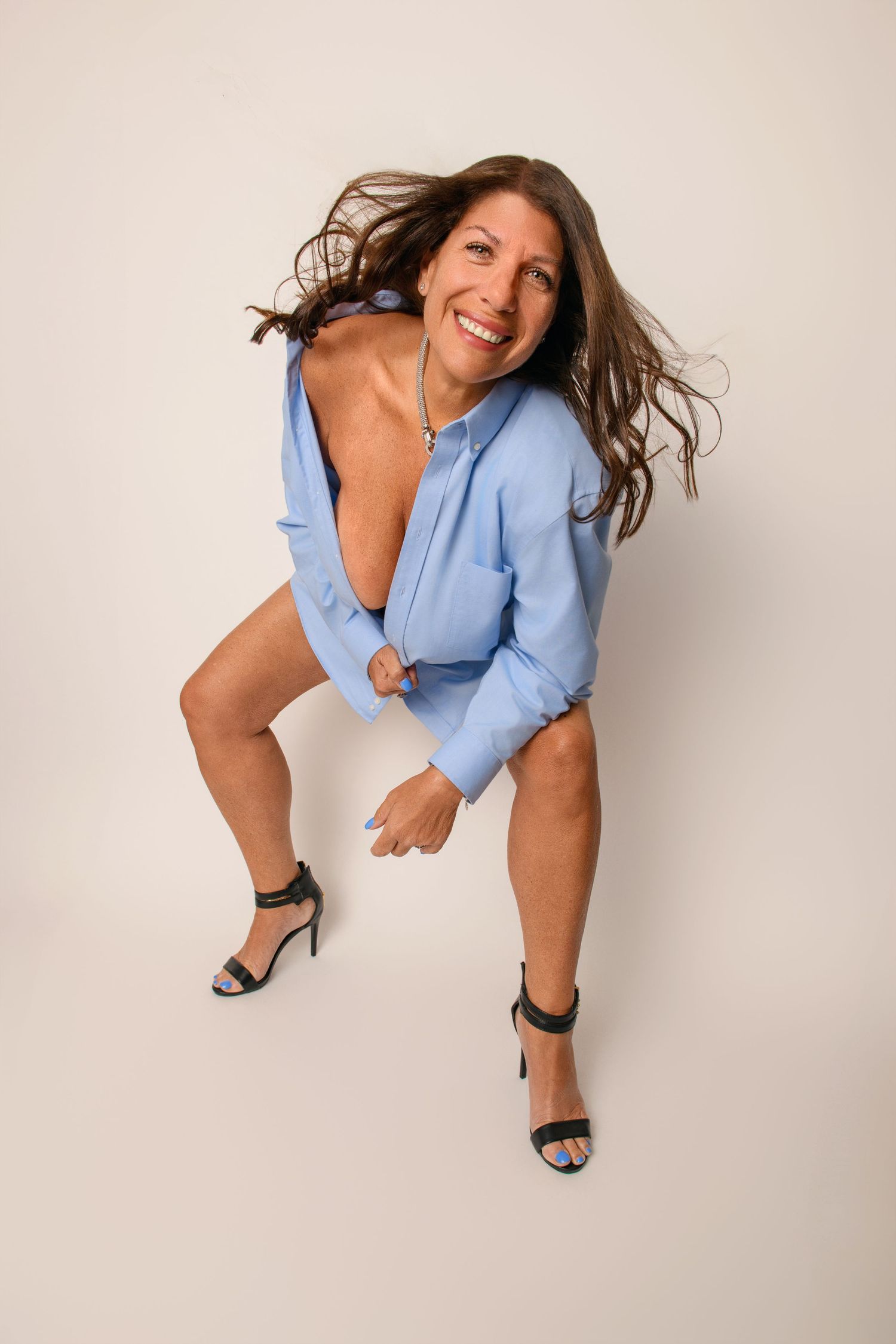 Playful fashion portrait of someone in light blue shirt and heels against white background.