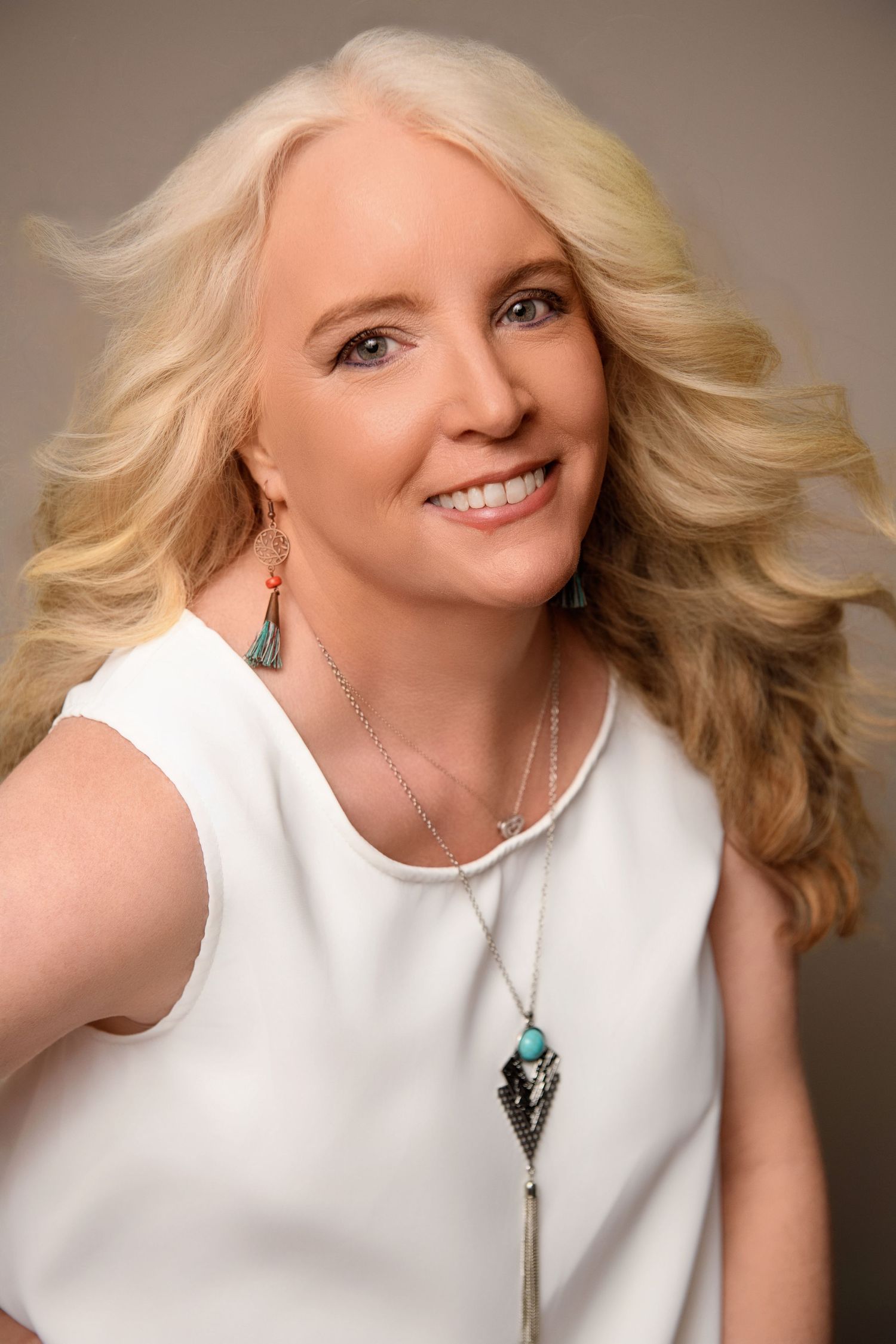 Portrait in white sleeveless top with turquoise statement necklace against neutral background.