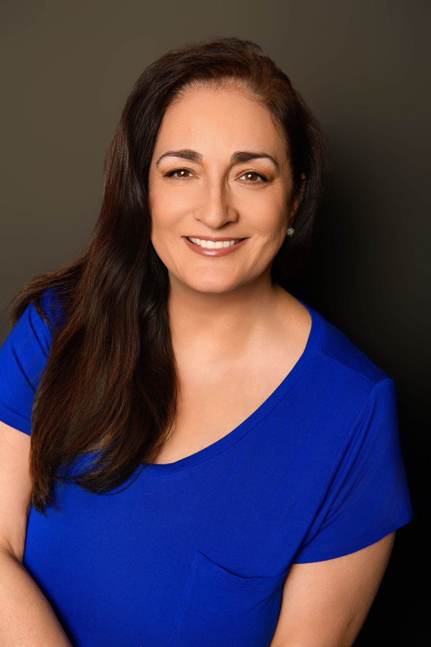 Warm professional portrait in royal blue top against dark background.