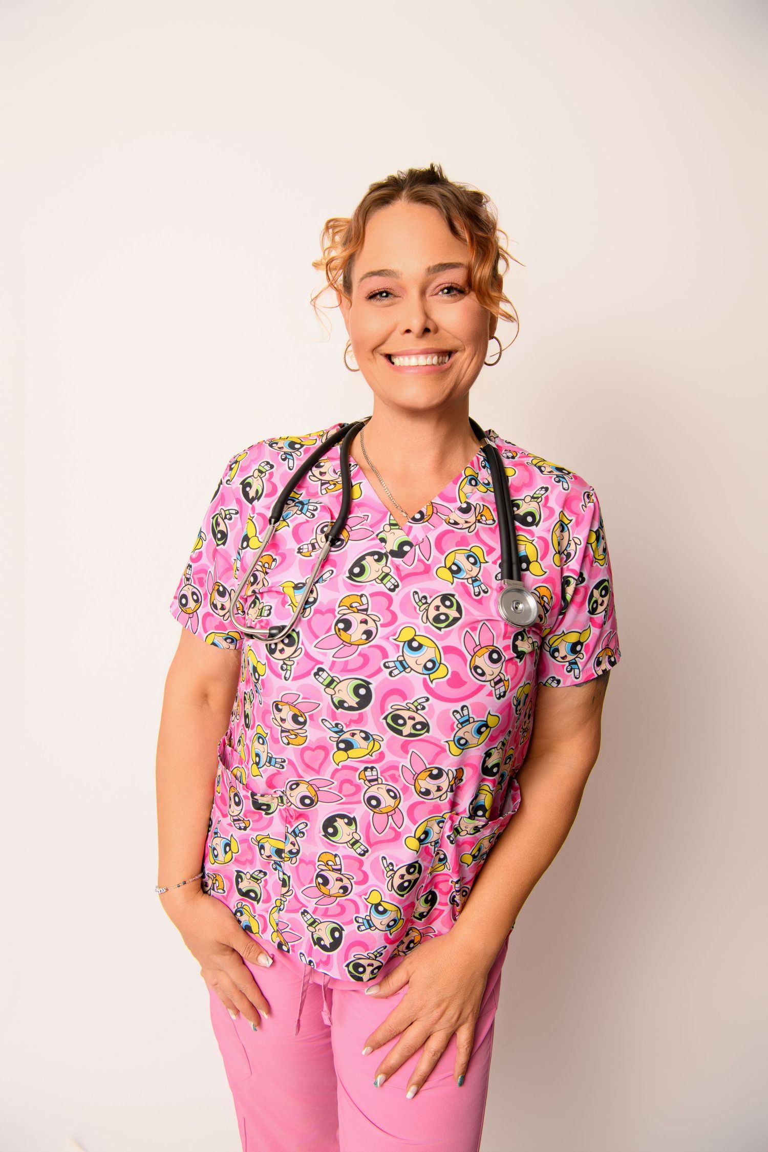 Medical professional in pink floral scrubs poses confidently with stethoscope and matching pants.
