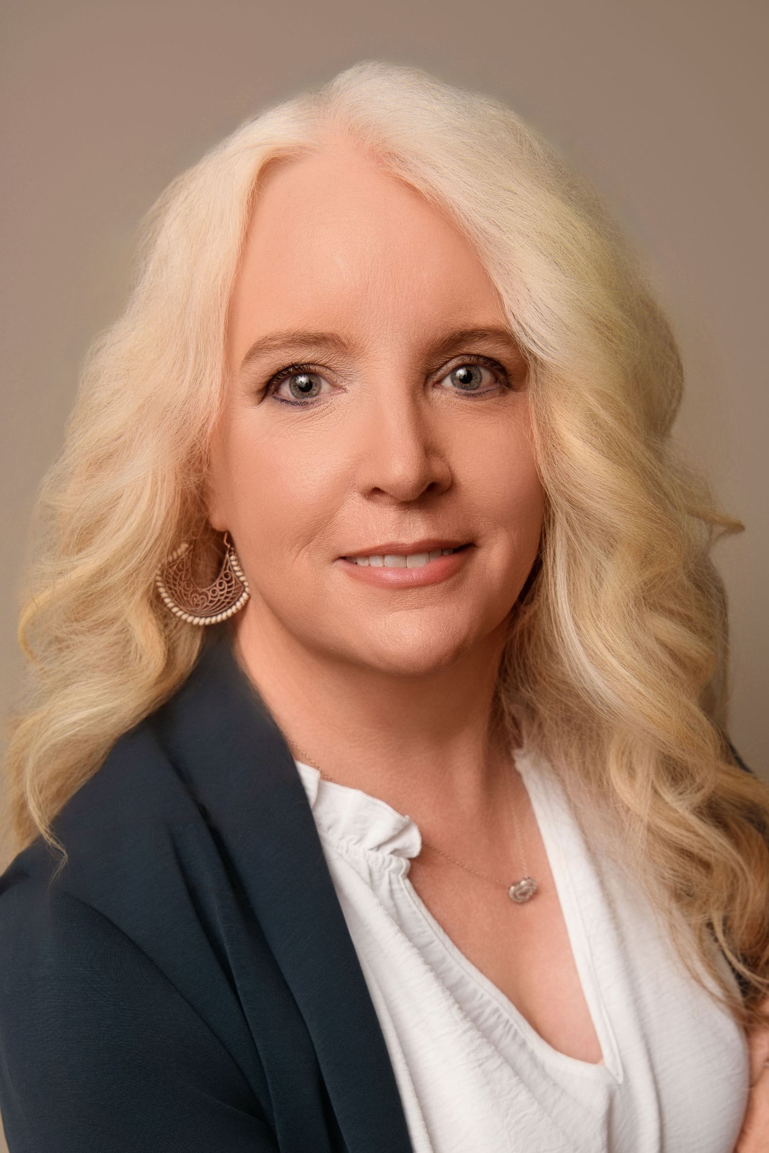 Professional headshot in navy blazer and white top with wavy styled hair.