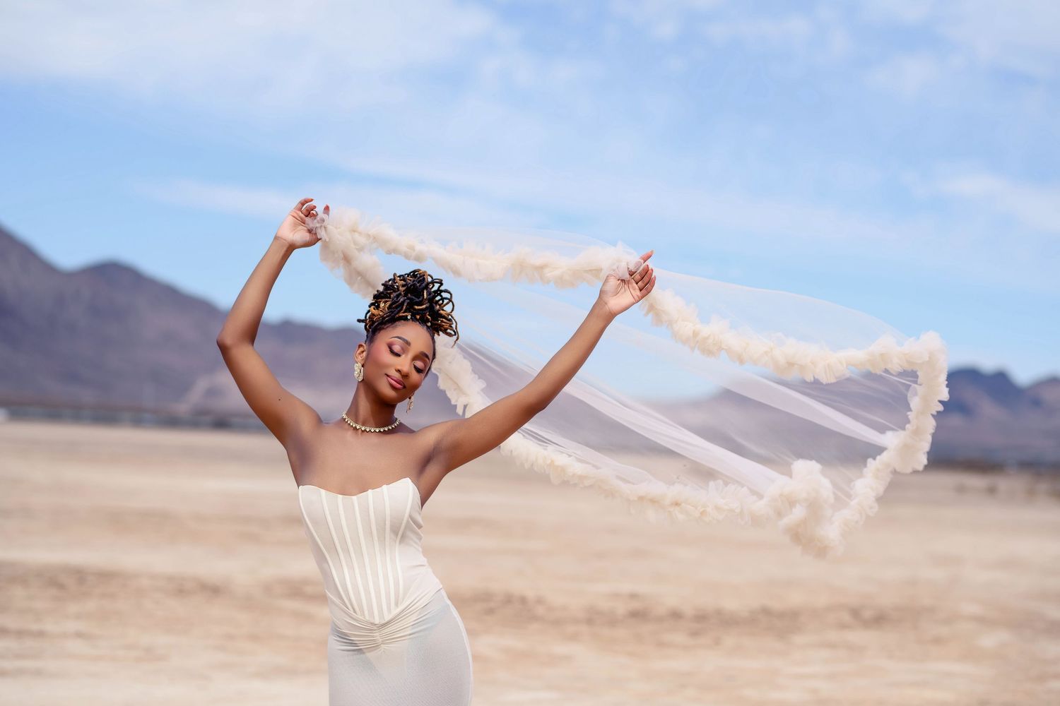 Joyful bridal portrait with flowing veil against desert mountain landscape.