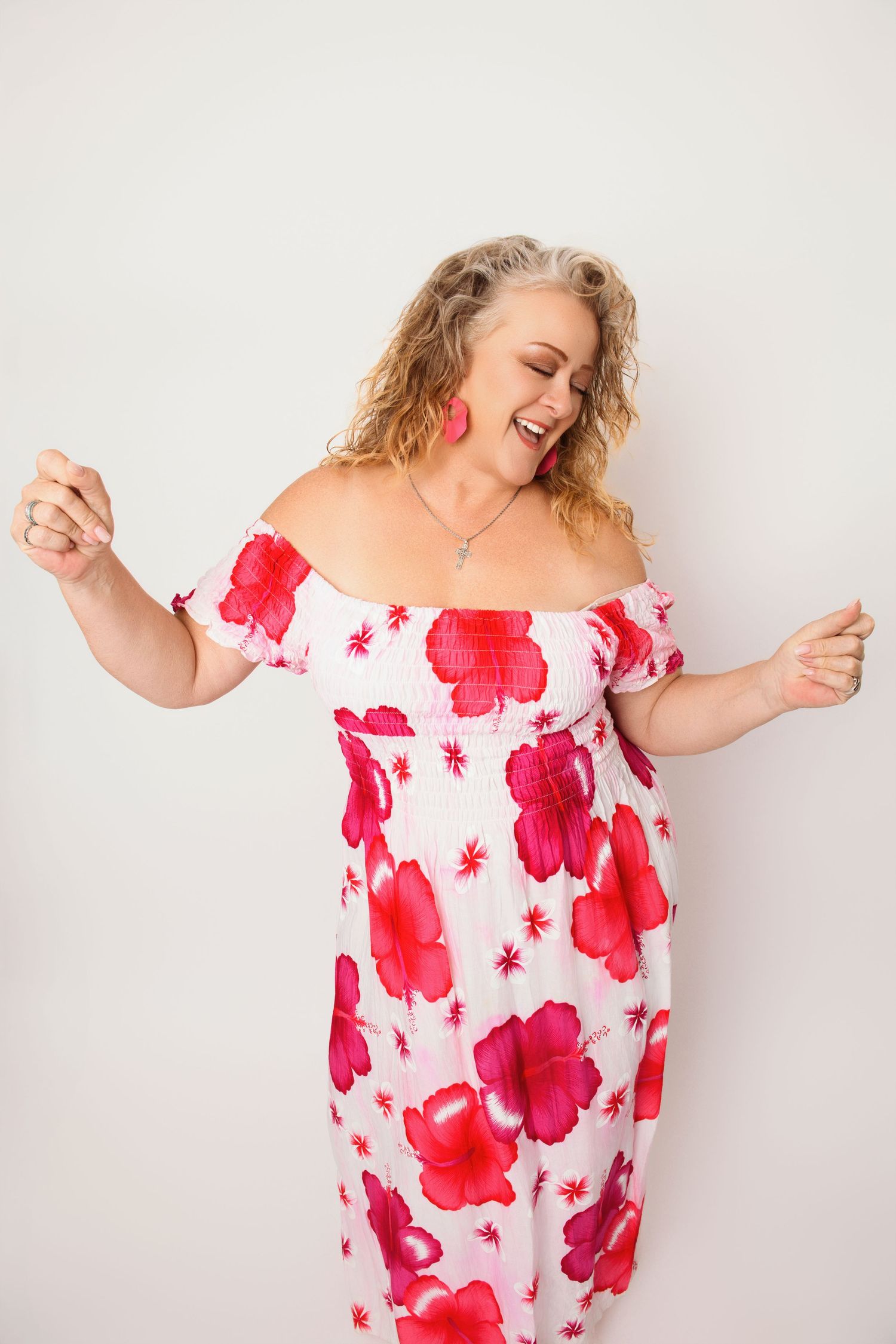 Joyful portrait in off-shoulder floral dress with red poppy print against white background.