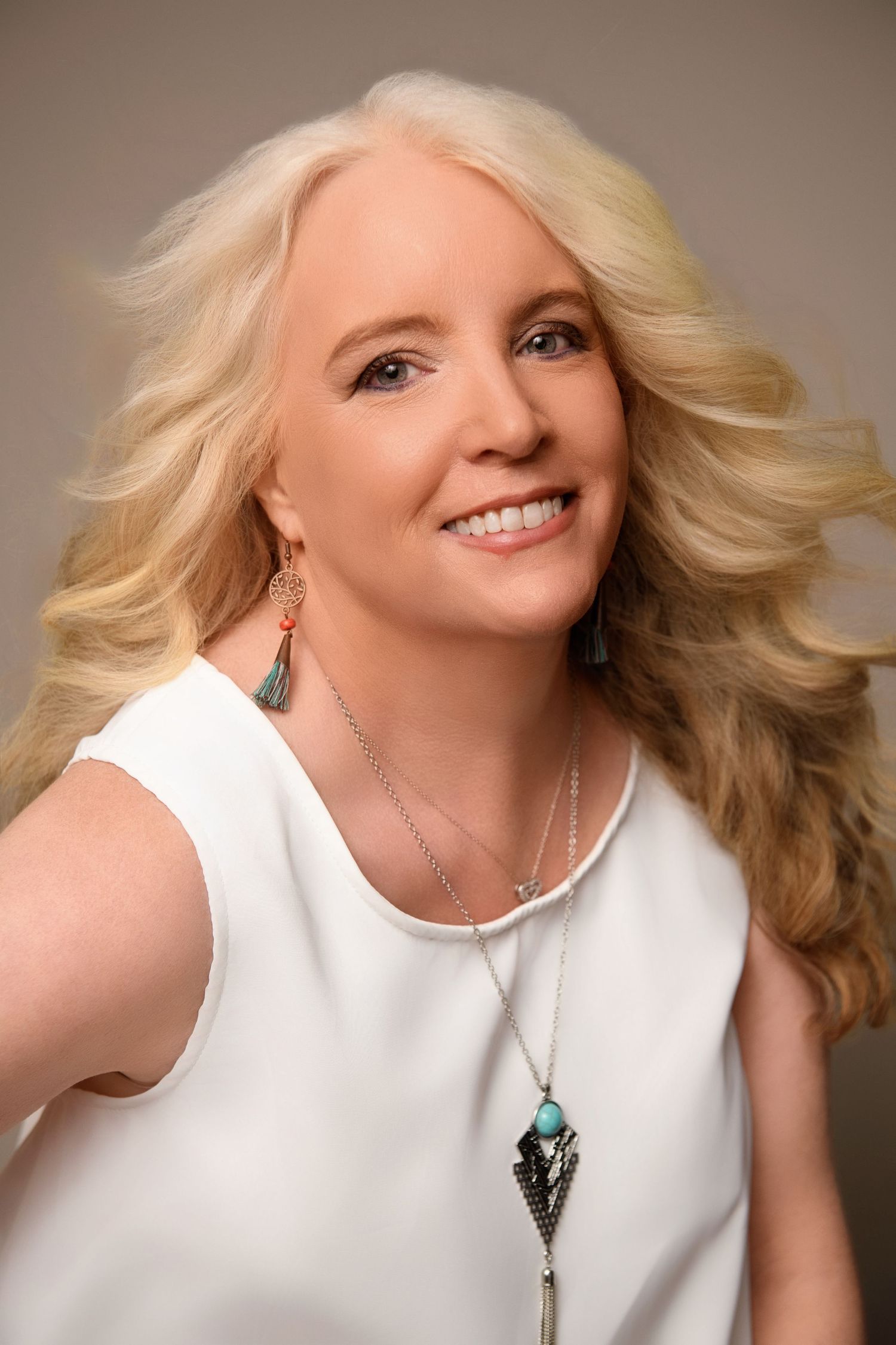 Studio portrait wearing white sleeveless top with long turquoise pendant necklace.
