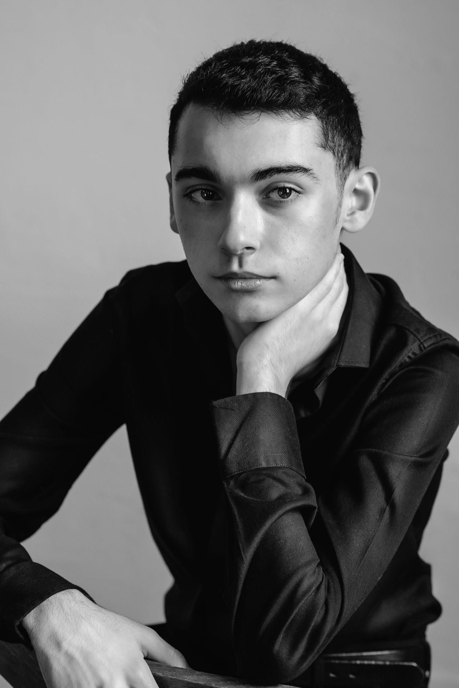 Dramatic monochrome portrait of person in dark shirt with hand posed thoughtfully near face.