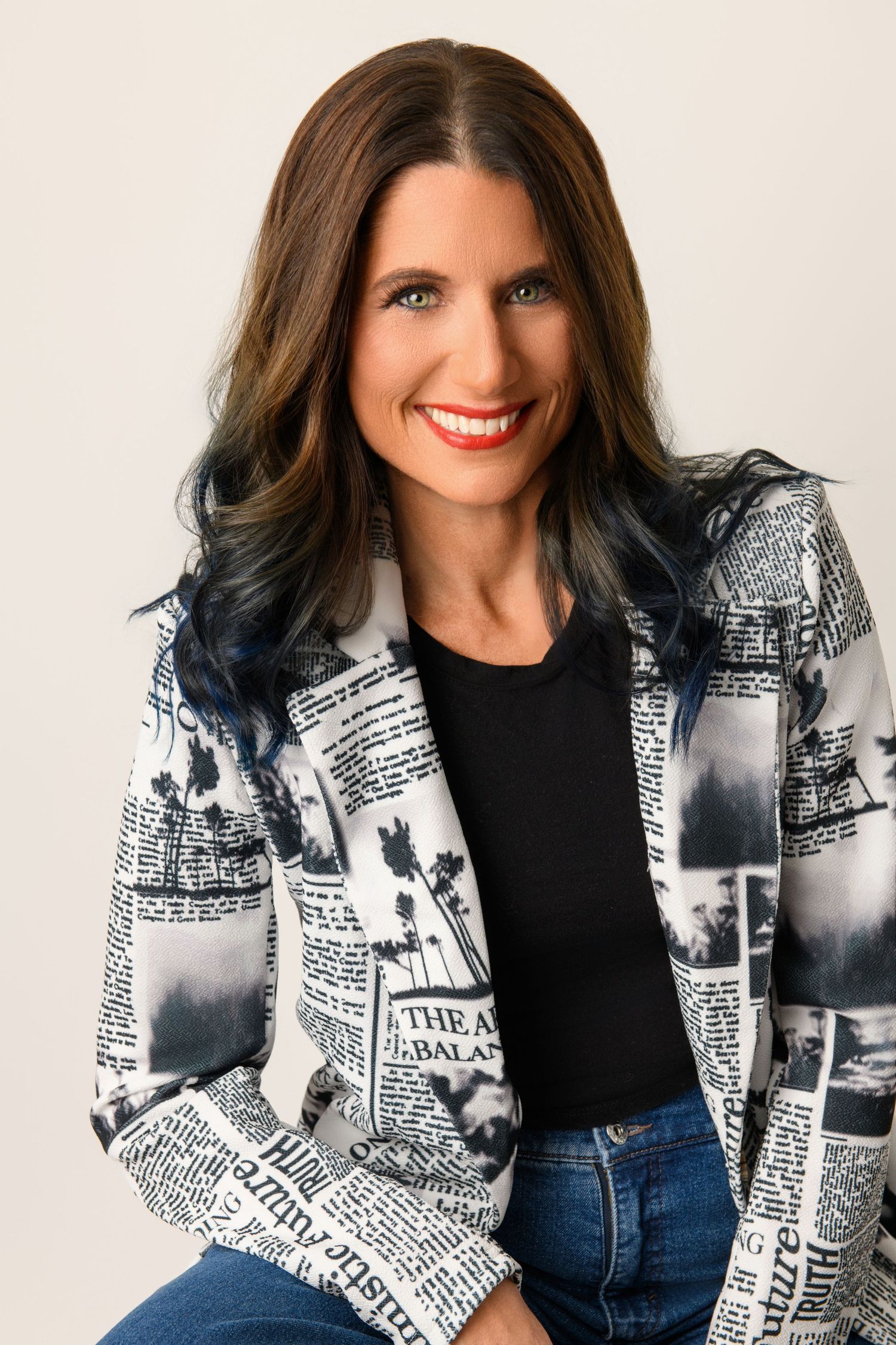 Professional portrait of someone wearing a black and white newspaper print blazer with jeans against a light background.