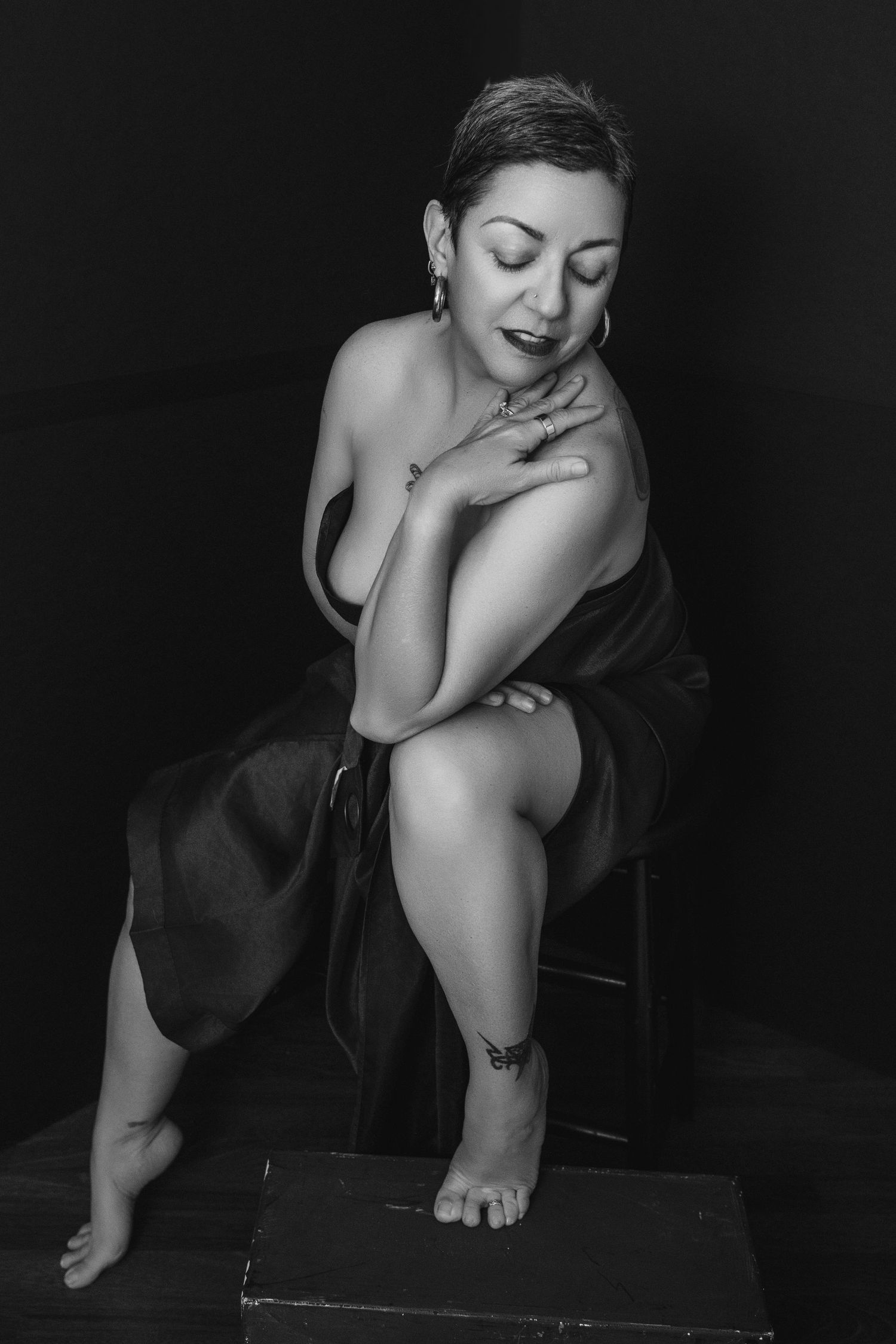 Moody black and white photo of a person in dark dress posing on wooden platform.