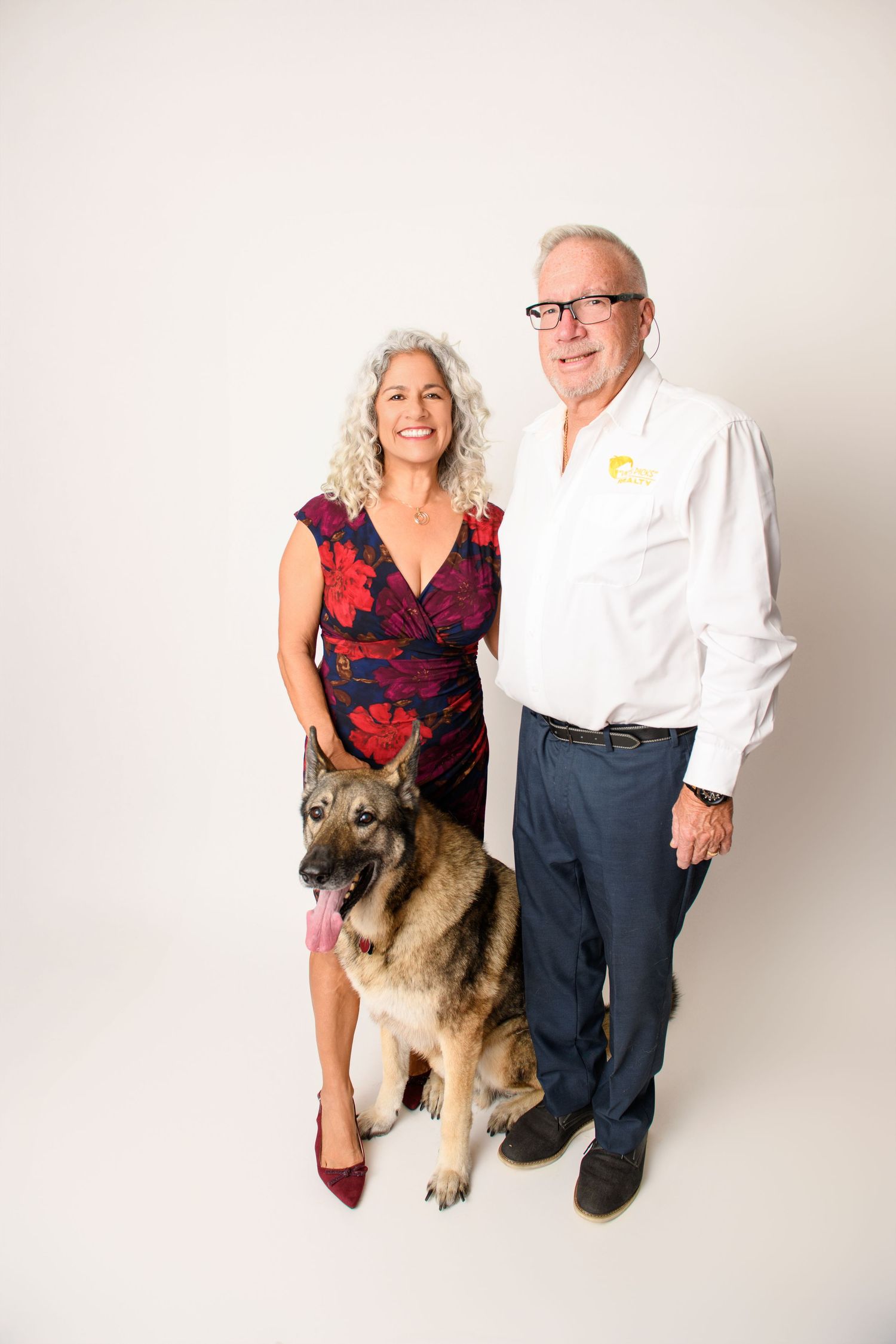 Professional studio portrait of a couple posing with their German Shepherd dog against a white background.