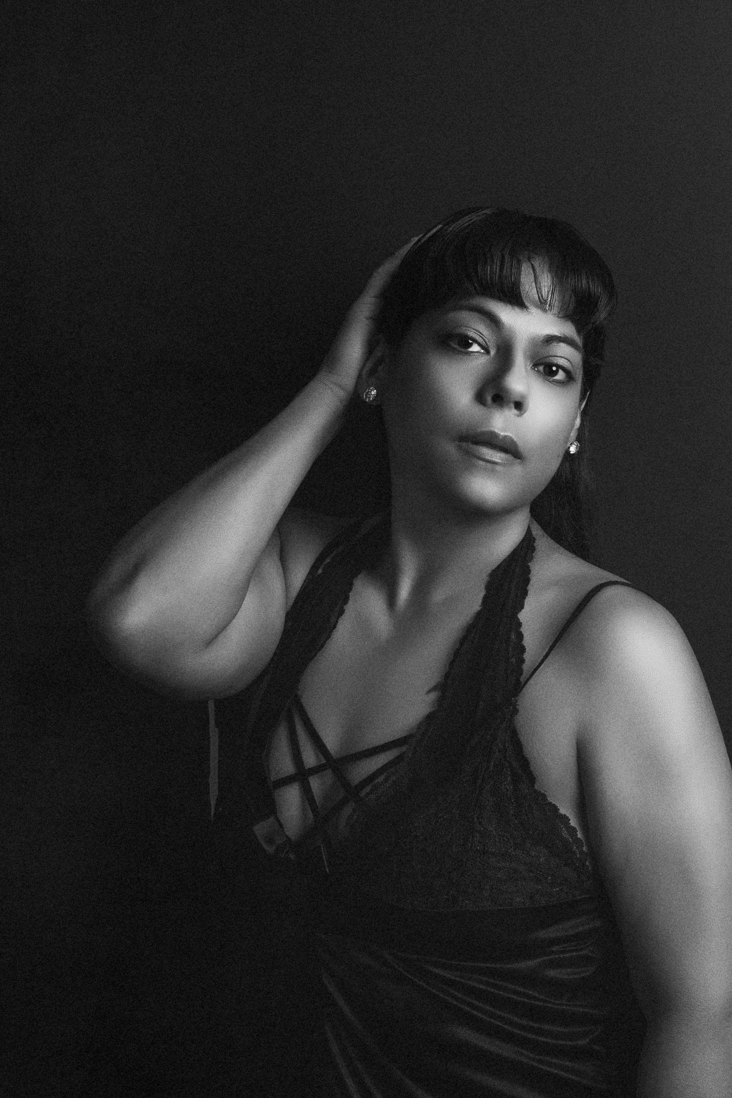 Dramatic black and white portrait featuring a model in a dark strappy top against dark background.