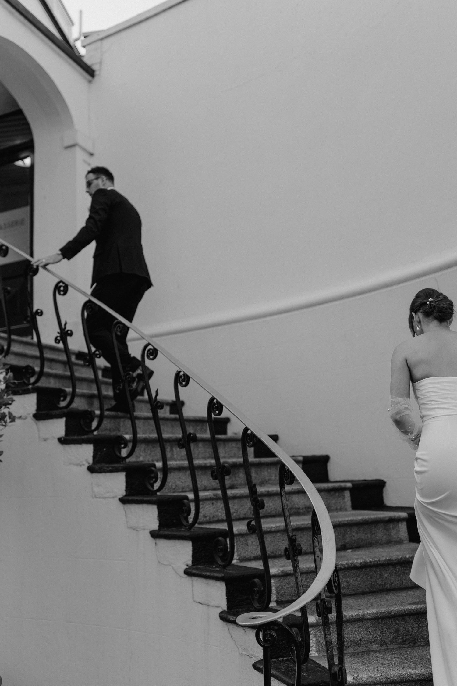 Couple ascending an elegant curved staircase in formal wedding attire.