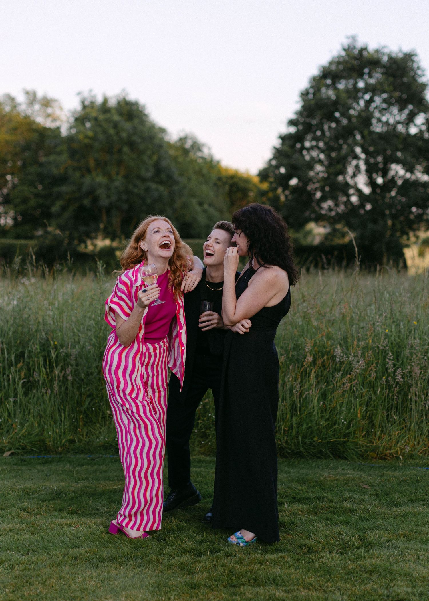 Two people laughing together in a grassy field during sunset.