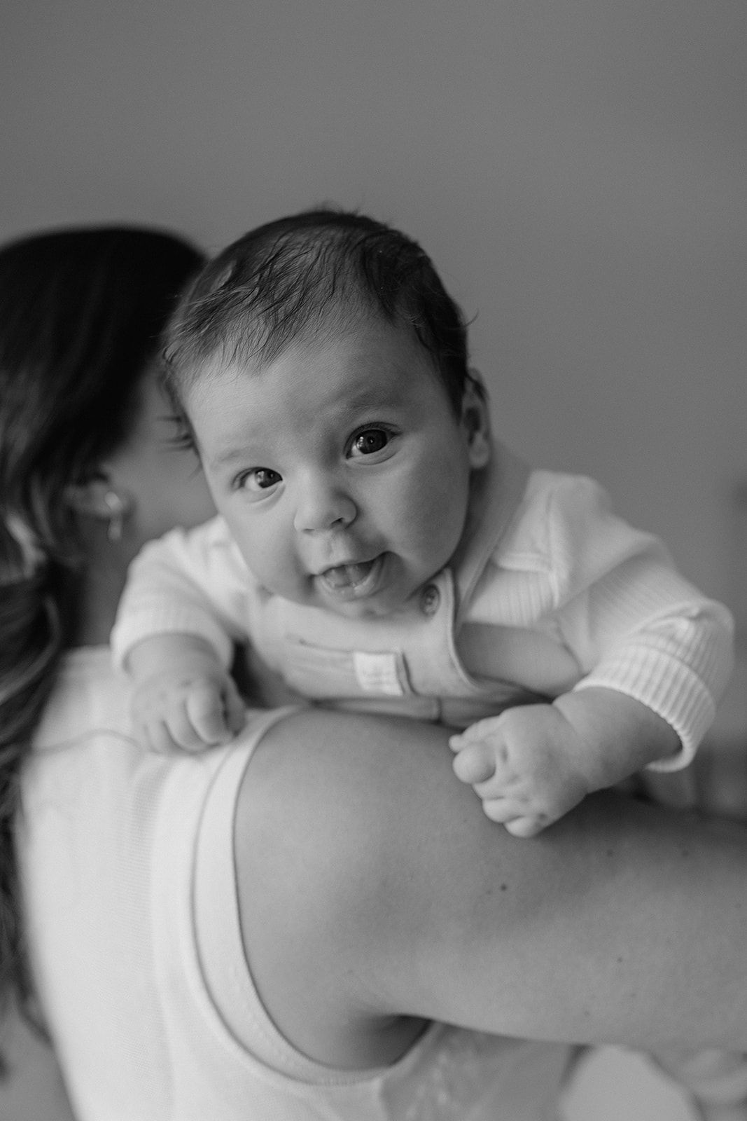 Black and white photo of a happy baby being held over a woman's shoulder, looking at the camera.