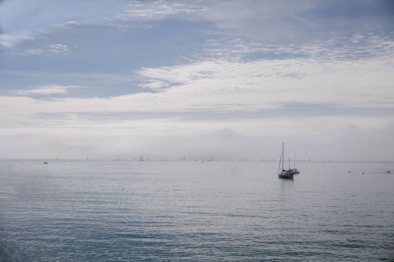 Serene seascape with distant sailboat under cloudy horizon.