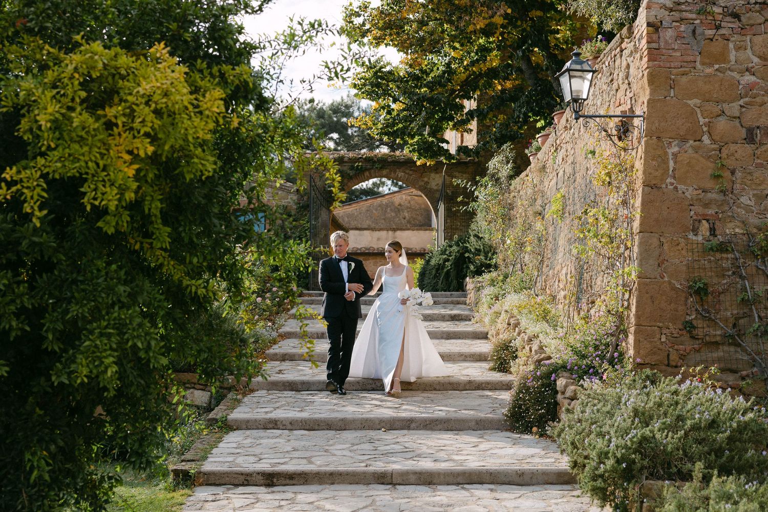 A stone pathway lined with greenery and trees leads through a rustic venue. Tuscany Wedding