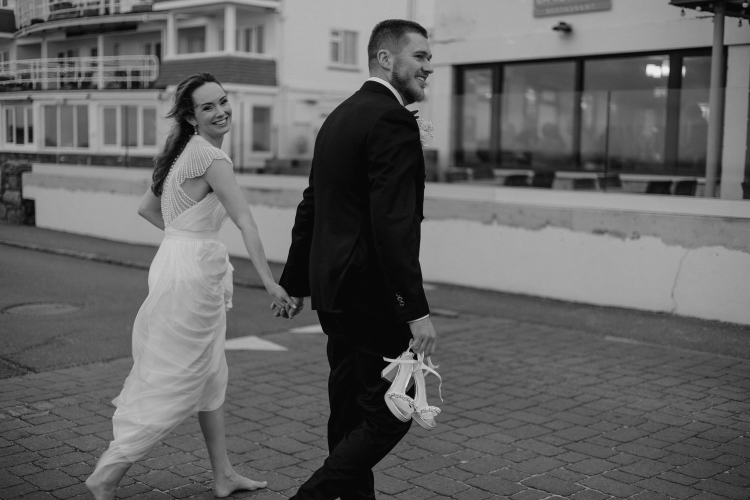 Newlyweds walking together on cobblestone street in black and white photography.