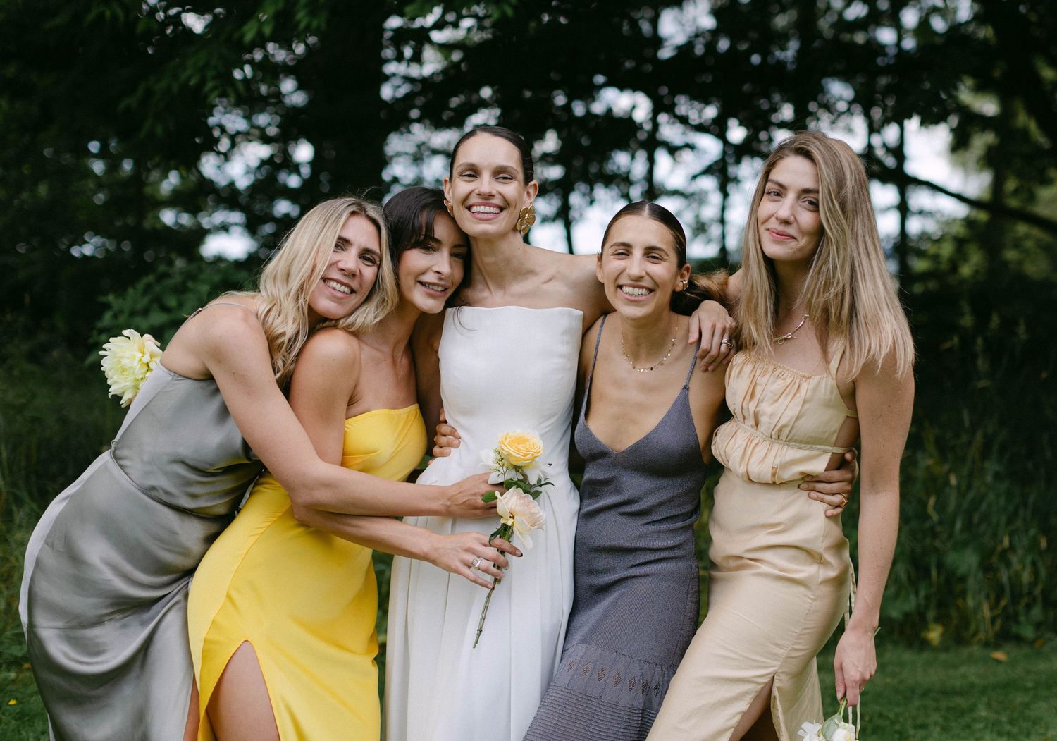 A group of bridesmaids in coordinating dresses pose together outdoors.