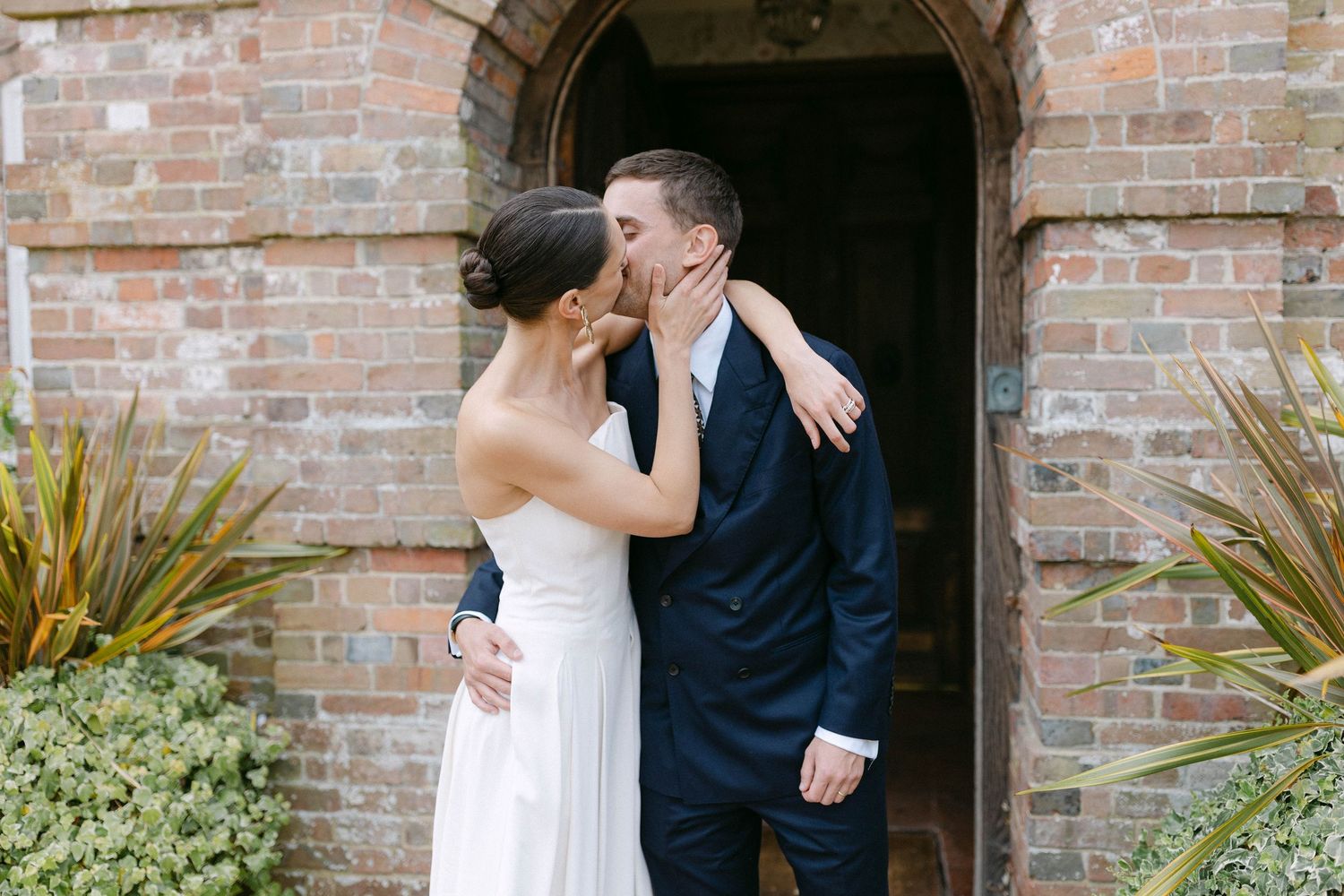 A couple shares an intimate moment against a rustic brick archway.