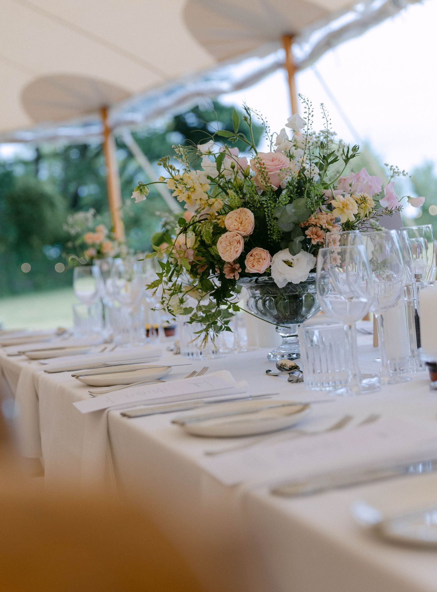 Elegant wedding table settings with floral centerpieces and glassware under white tent.