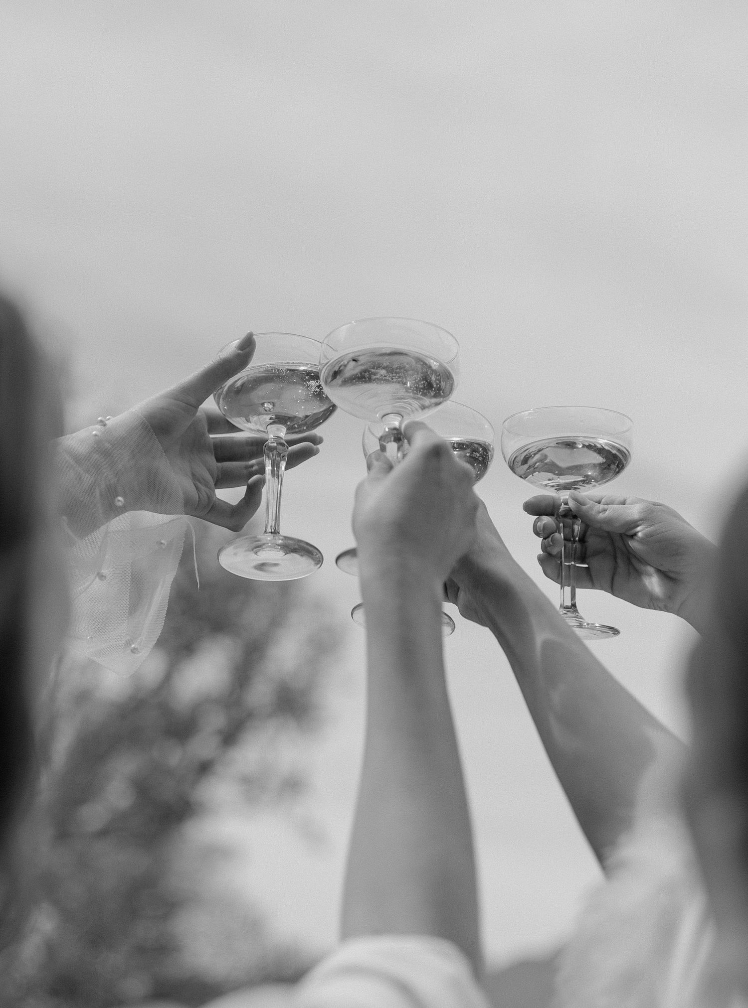 Black and white image of raised champagne glasses in a celebratory toast.