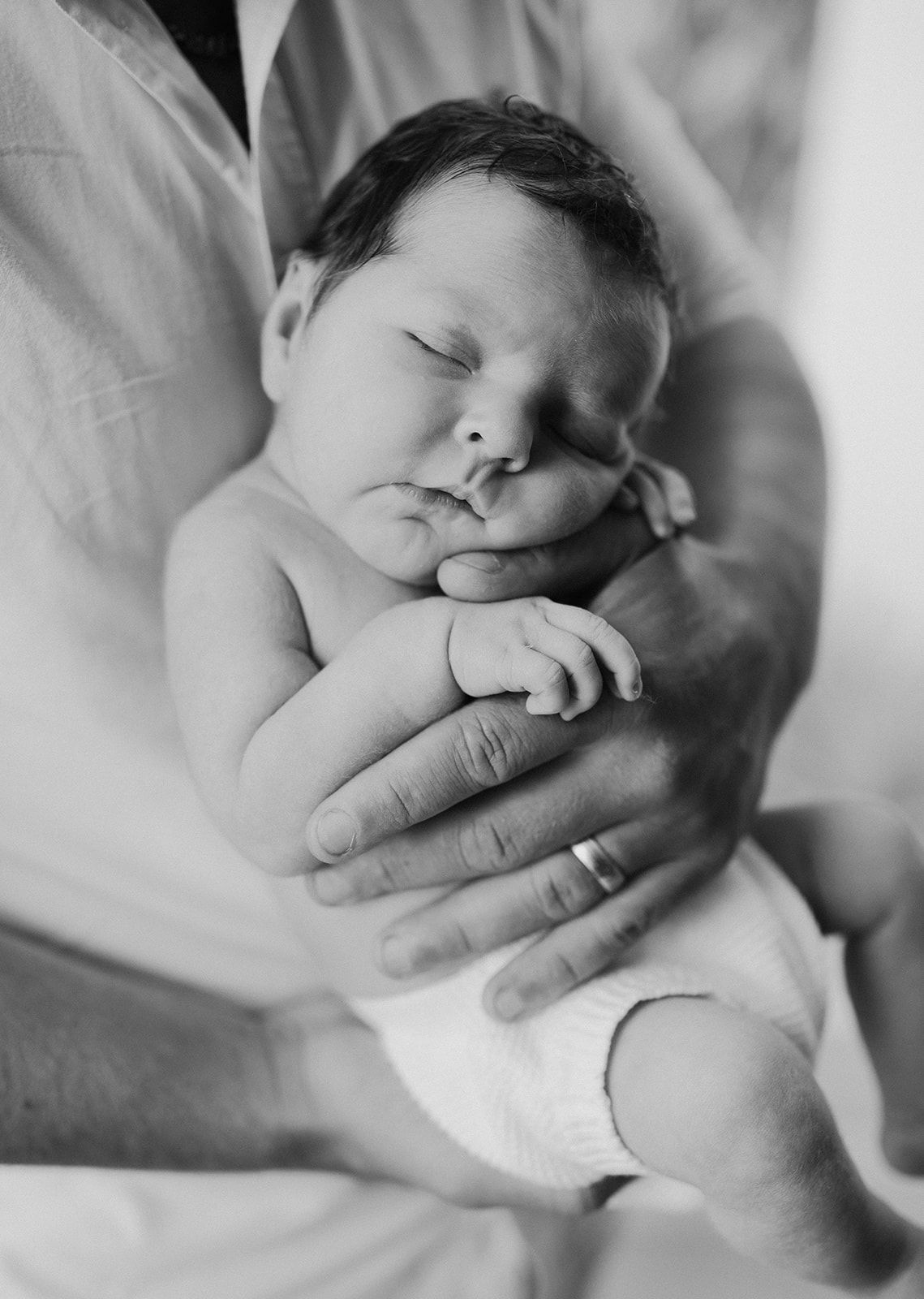 Black and white photo of a sleeping newborn baby cradled in an adult's hands, wearing a diaper.