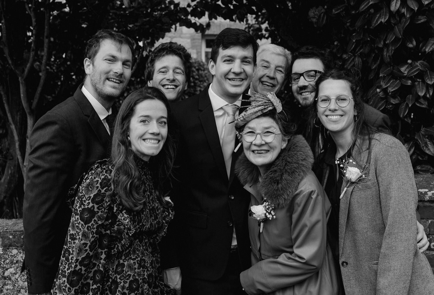Black and white group photo of wedding guests sharing joyful moments outdoors.