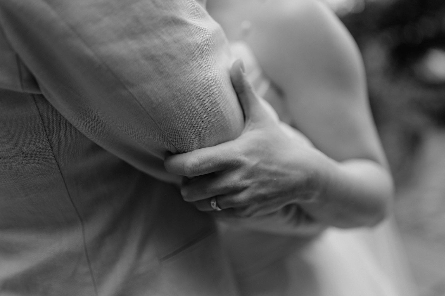 Intimate black and white close-up of couple holding hands during wedding ceremony.