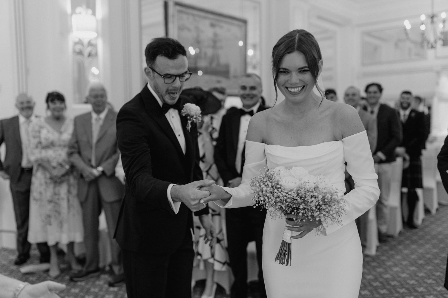 Elegant wedding ceremony in a grand ballroom with an off-shoulder white dress and formal attire.