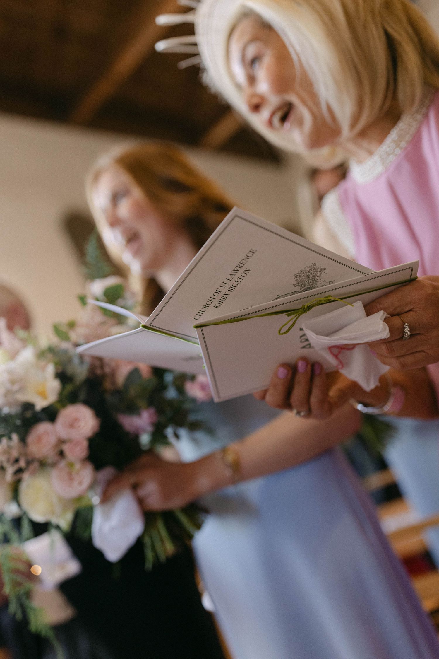 Wedding guests hold ceremony programs and floral arrangements in soft pastel colors.