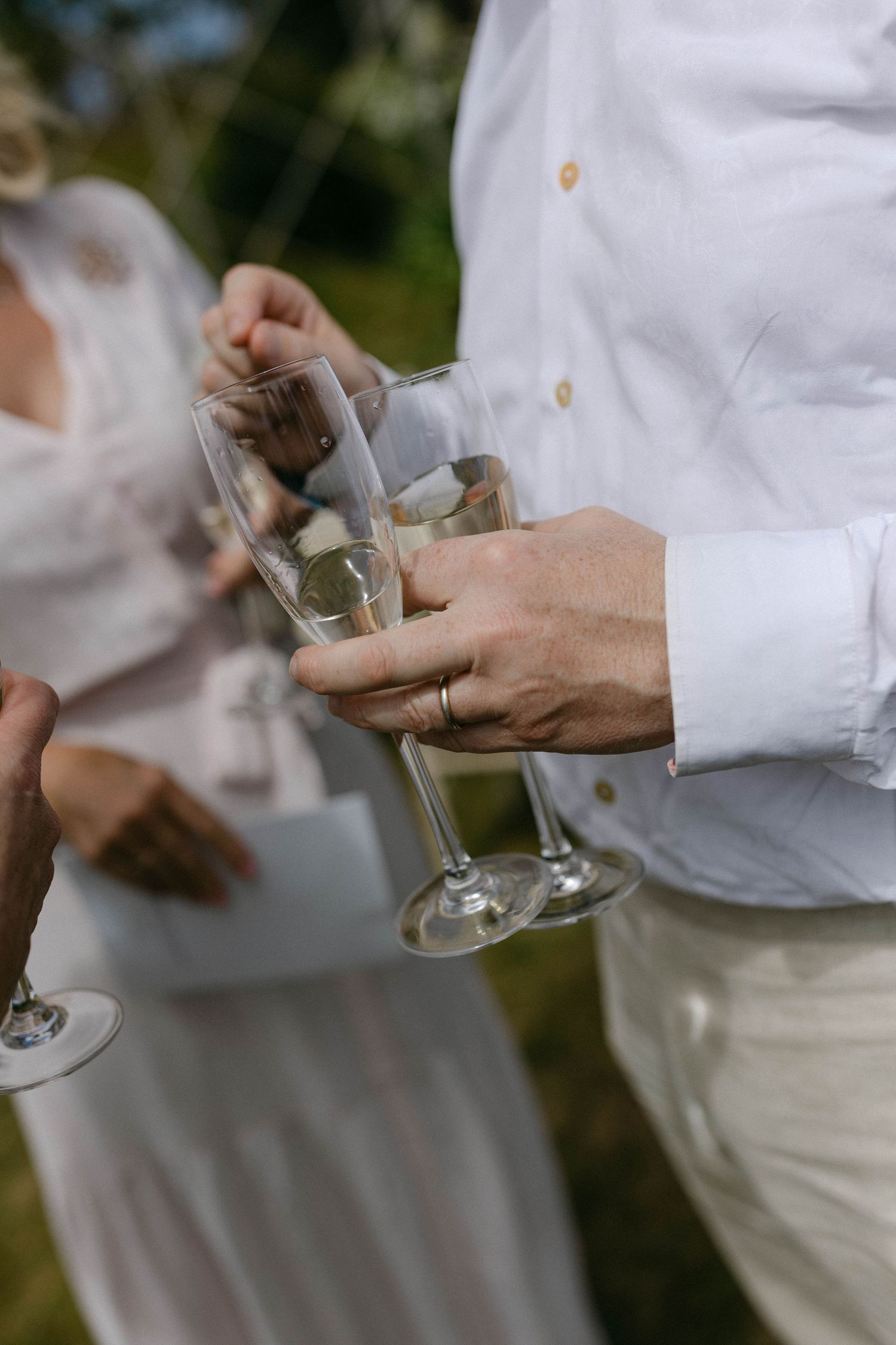 Hands holding champagne glasses during an outdoor wedding celebration.
