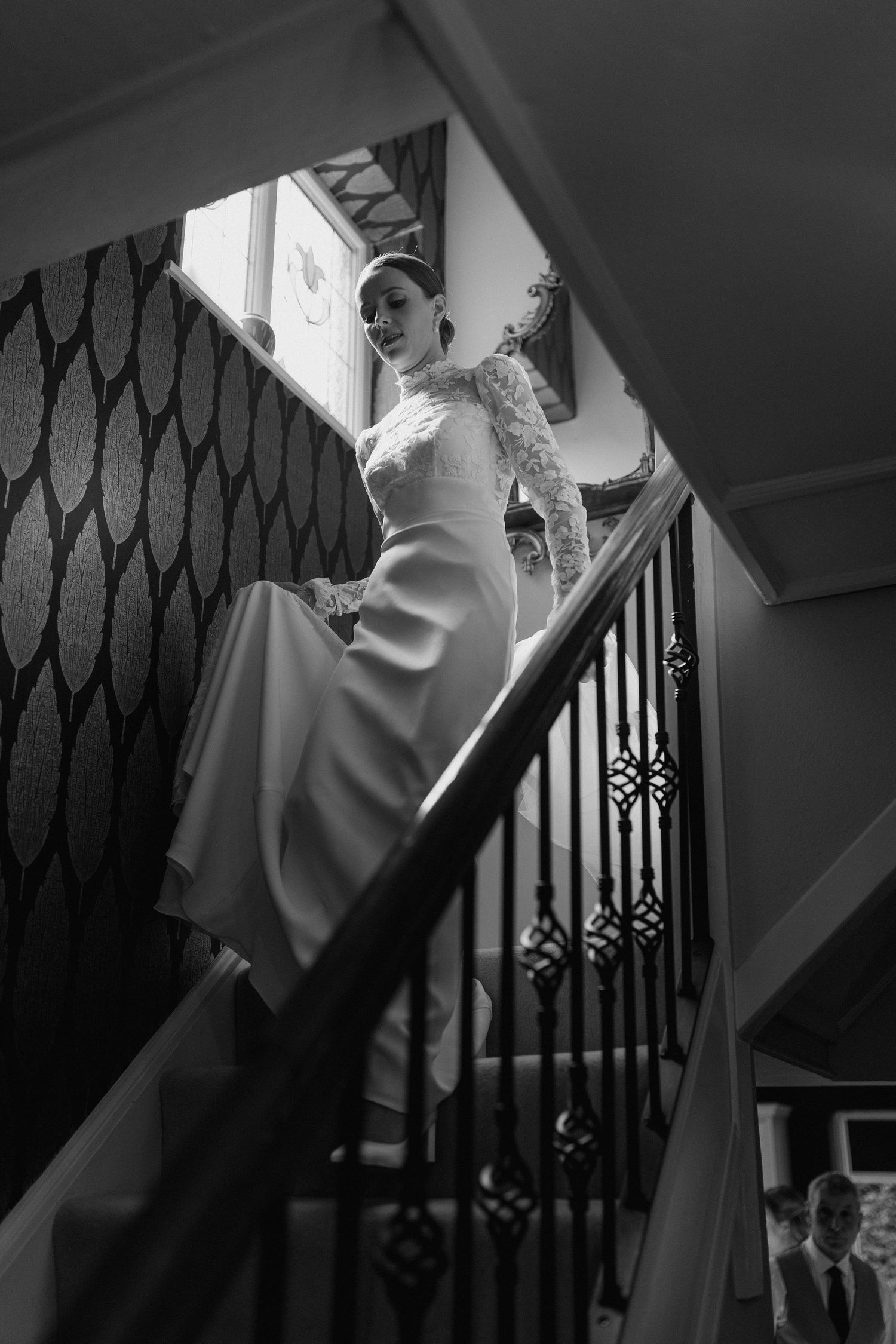 Dramatic black and white photo of a bride in a fitted gown descending an elegant staircase.