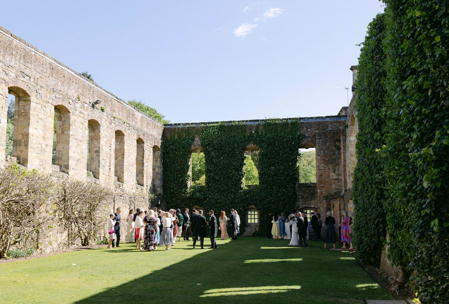 Wedding guests gather in a historic stone courtyard with ivy-covered walls.