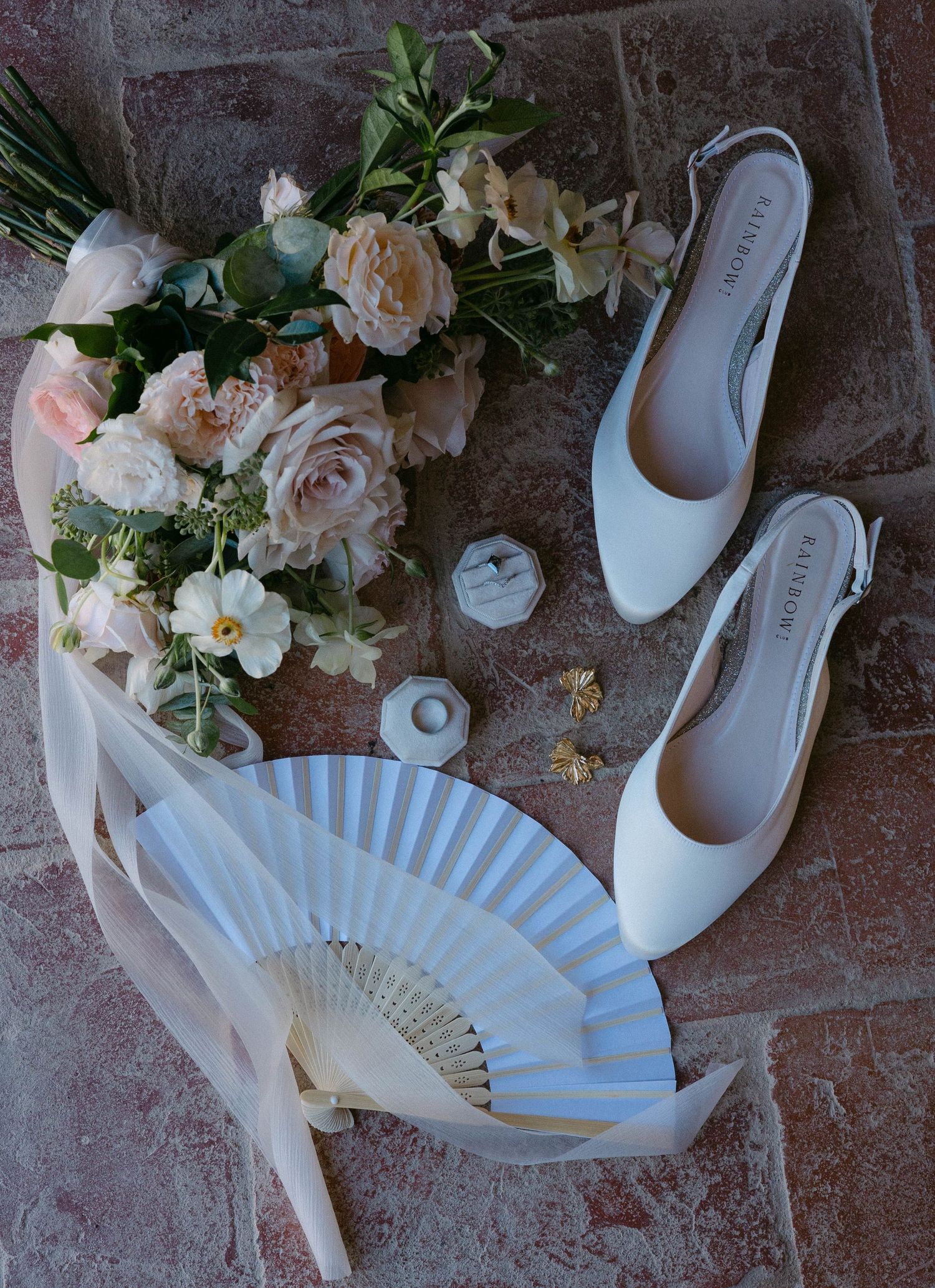 Wedding accessories including white shoes, a decorative fan and delicate floral bouquet.