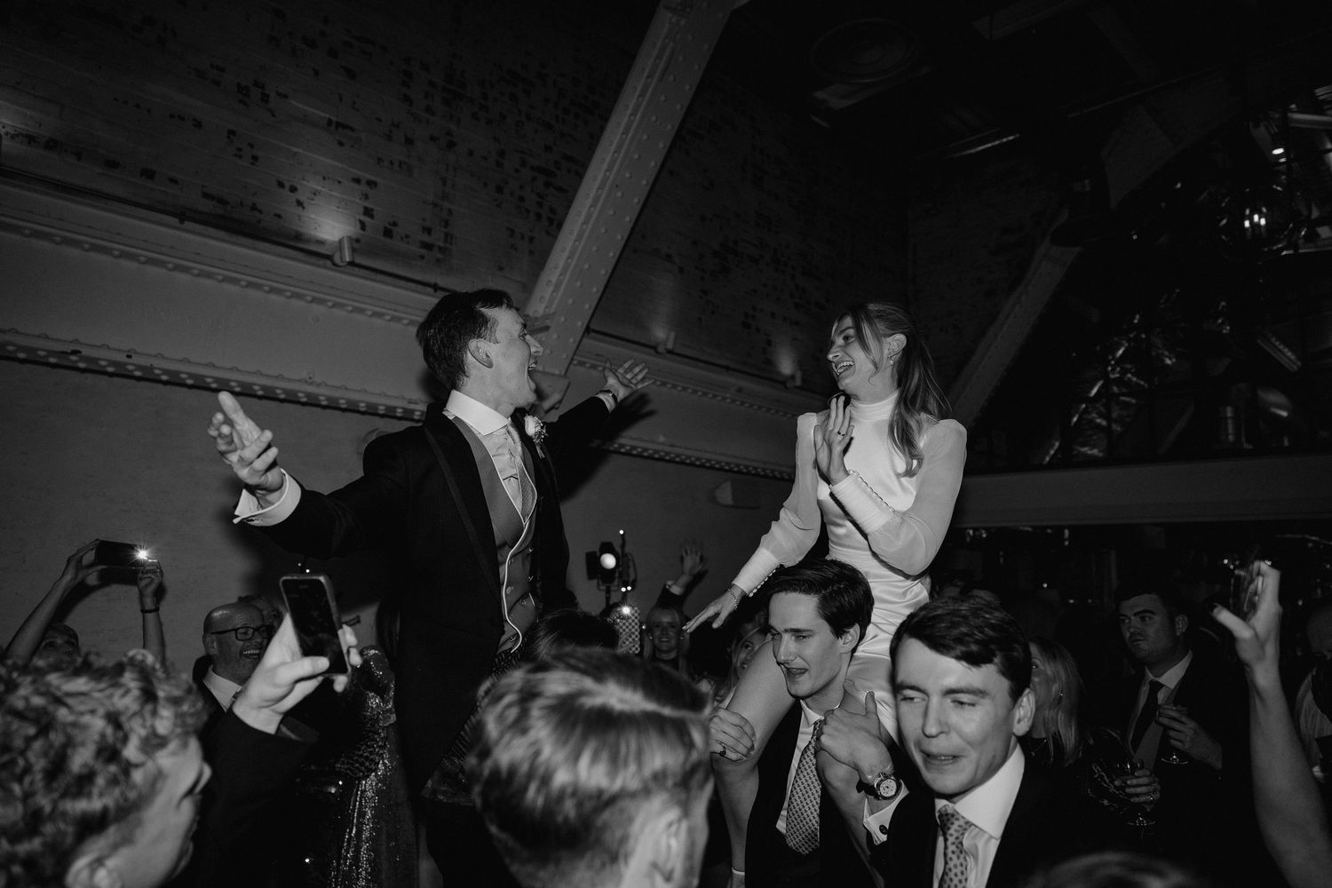 Wedding reception dance floor filled with guests celebrating in a dimly lit venue.