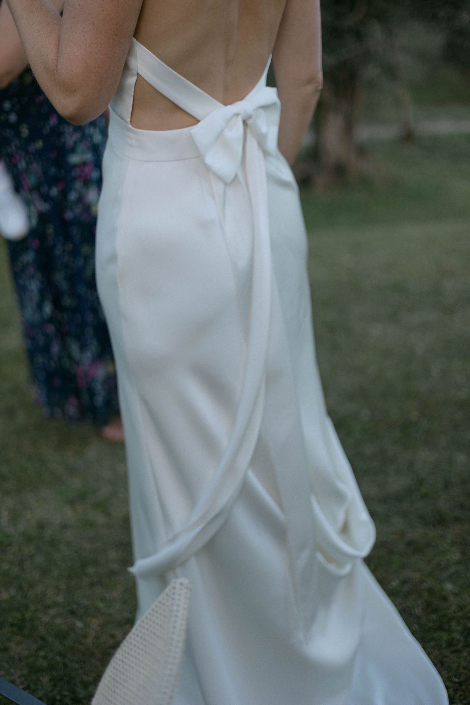 Close-up details of an elegant white wedding dress with pearl embellishments against a natural outdoor background.