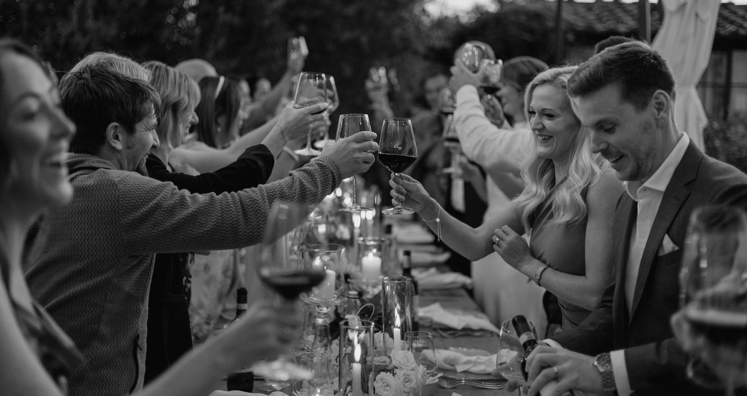 Black and white candid shot of wedding reception guests enjoying dinner outdoors.