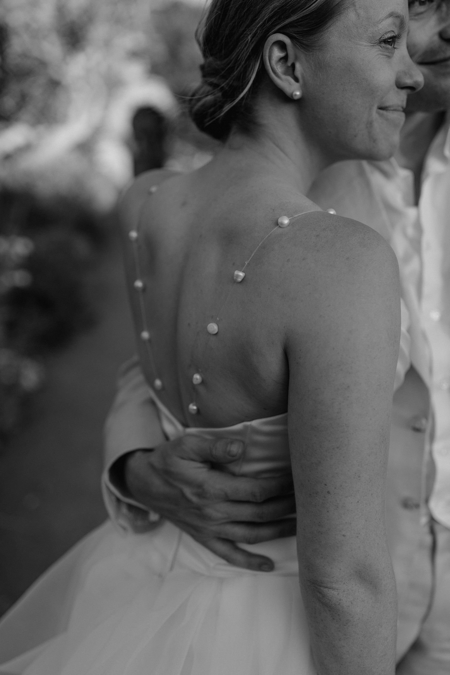Close-up black and white photo showing the back detail of a wedding dress with delicate buttons down the spine.