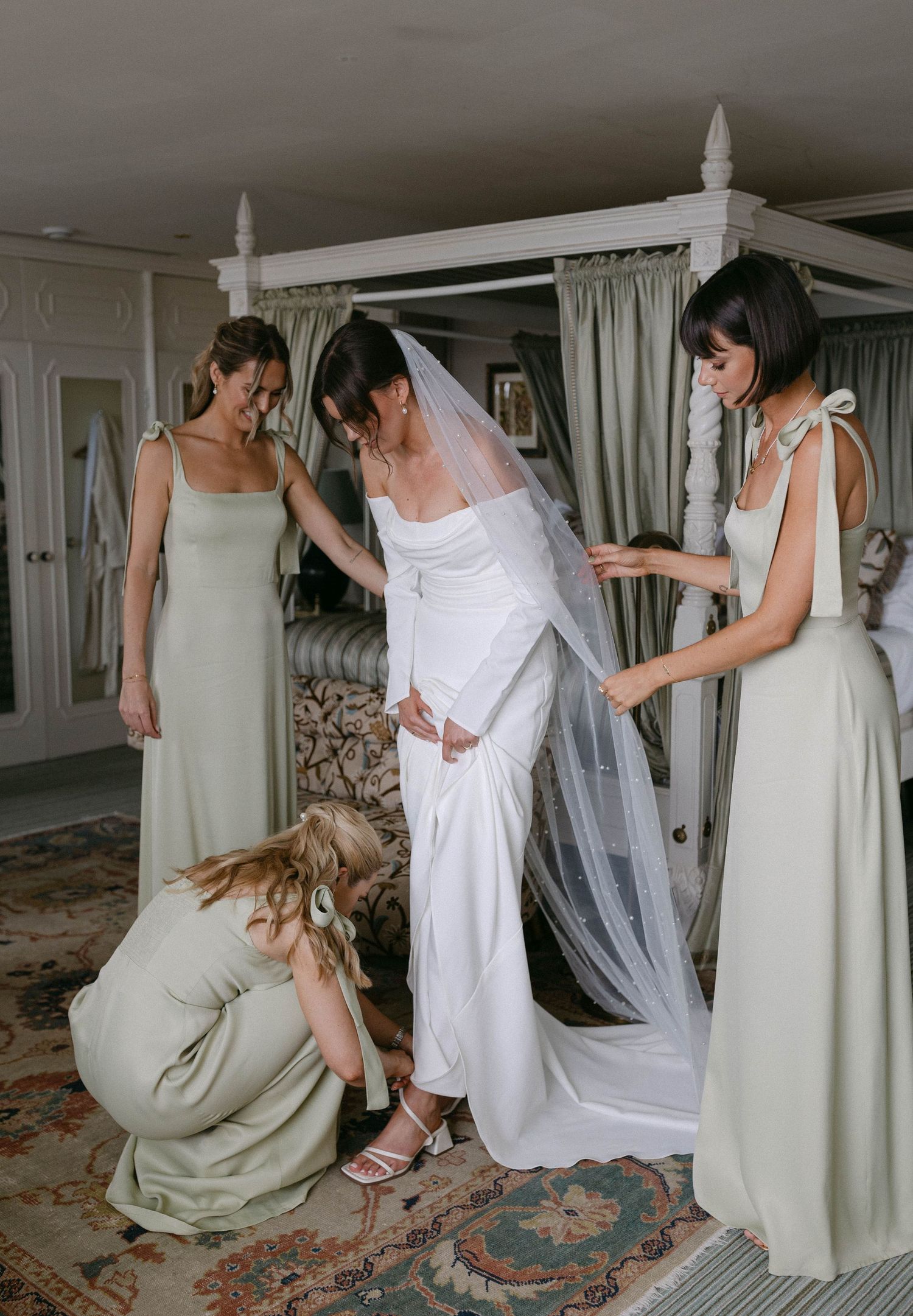 A bride getting ready in a white dress as helpers assist with final adjustments.