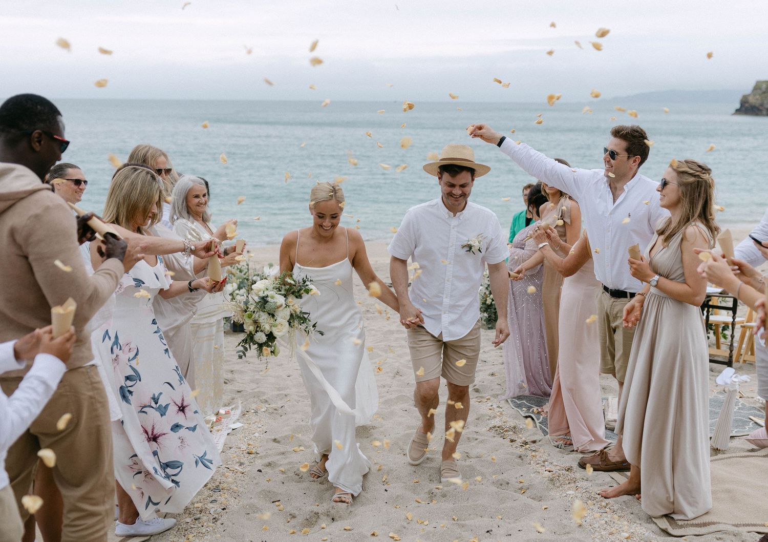 Wedding celebration on a beach with guests throwing flower petals in a joyful moment.