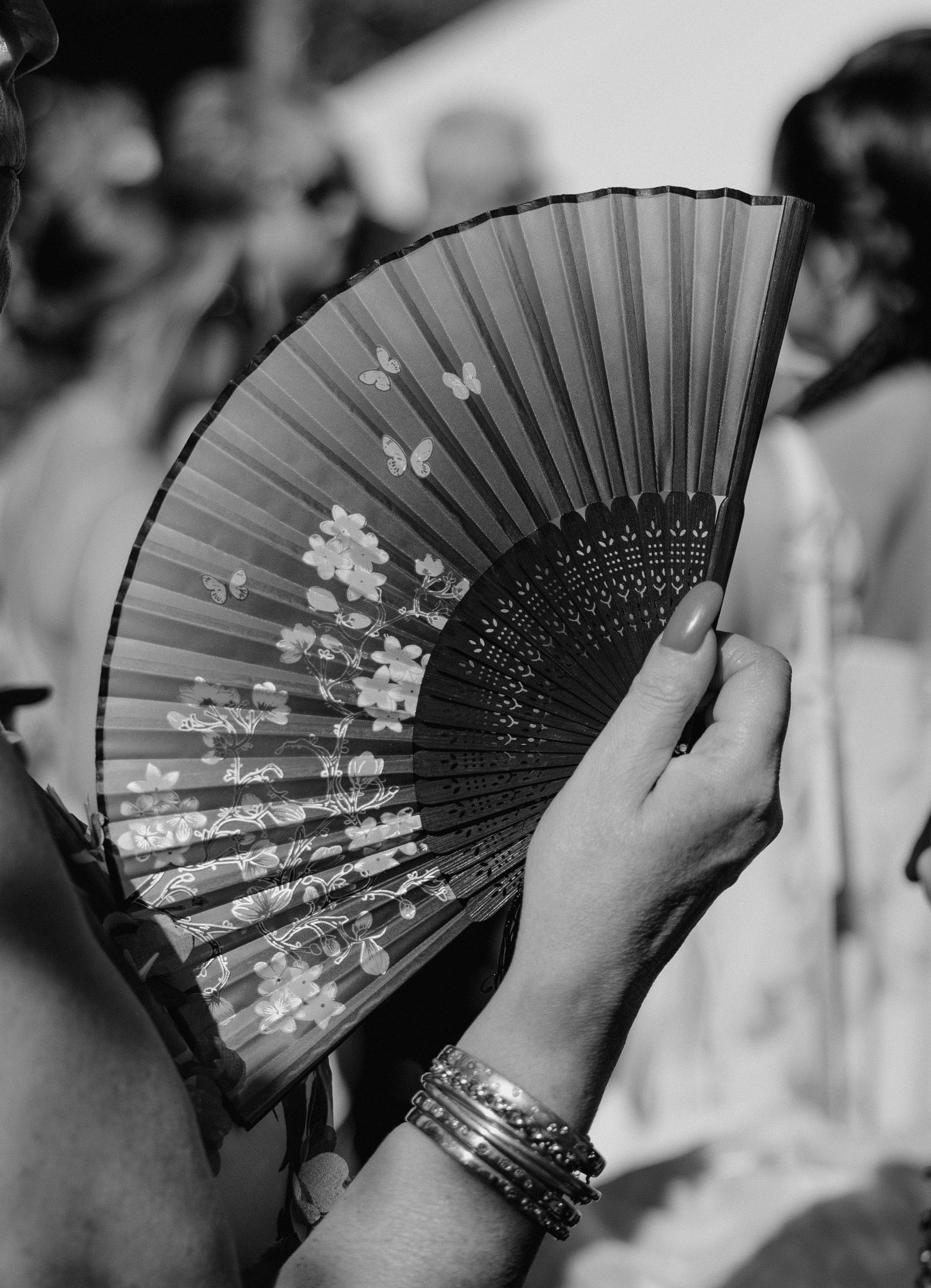 Decorative black and white folding fans with floral designs being held at a wedding.