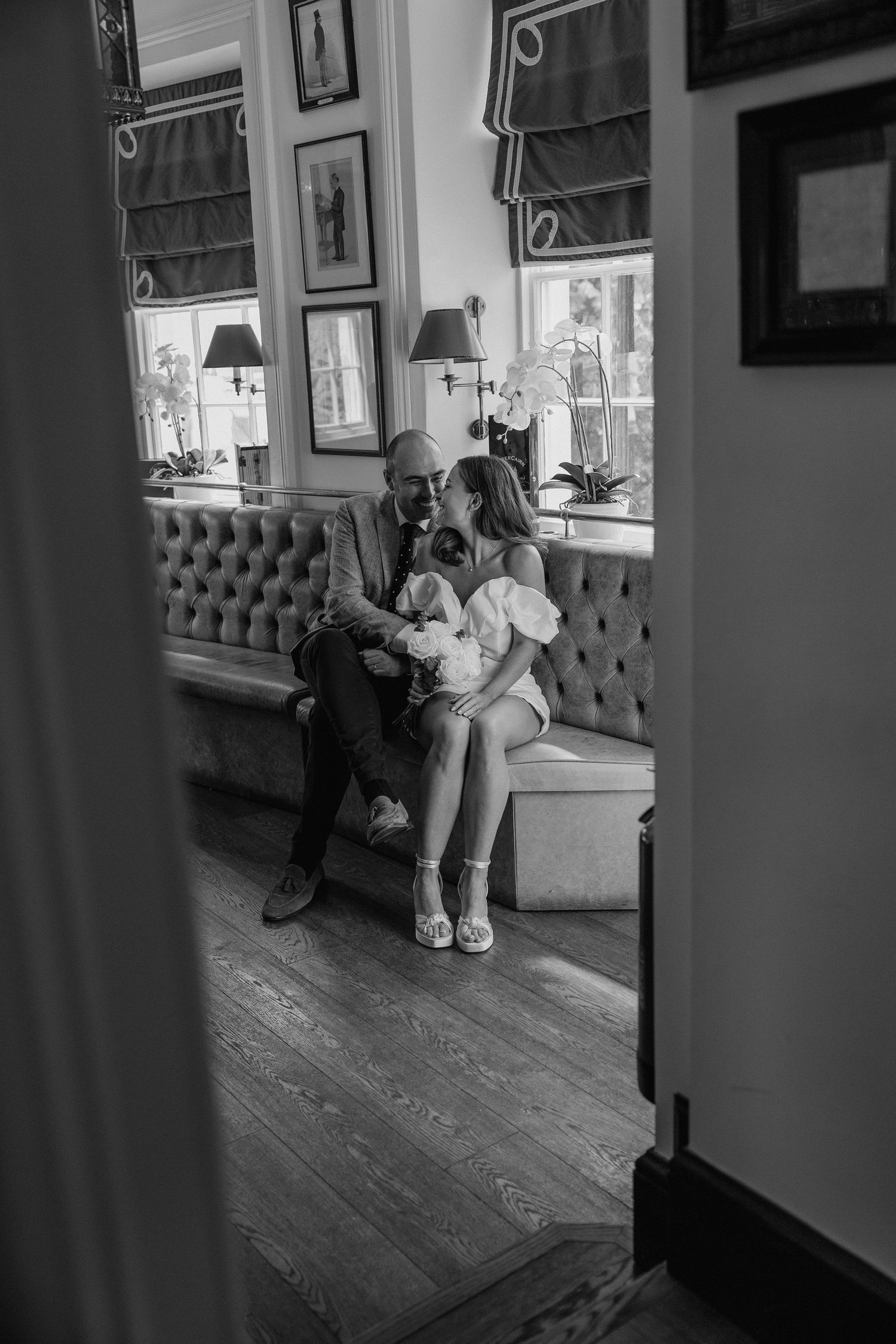 An intimate moment captured through a doorway showing a couple seated on an elegant tufted bench.