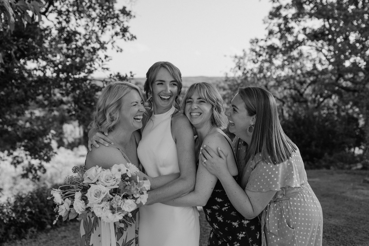Bridesmaids share an emotional group hug in black and white photography.