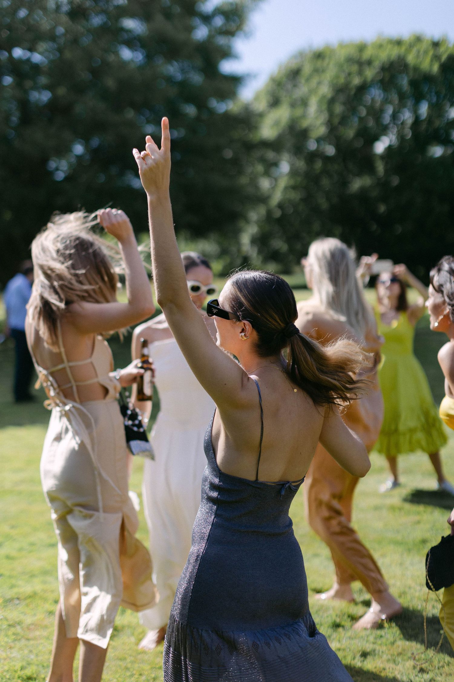 Wedding guests dancing and celebrating with raised arms outdoors on a sunny day.