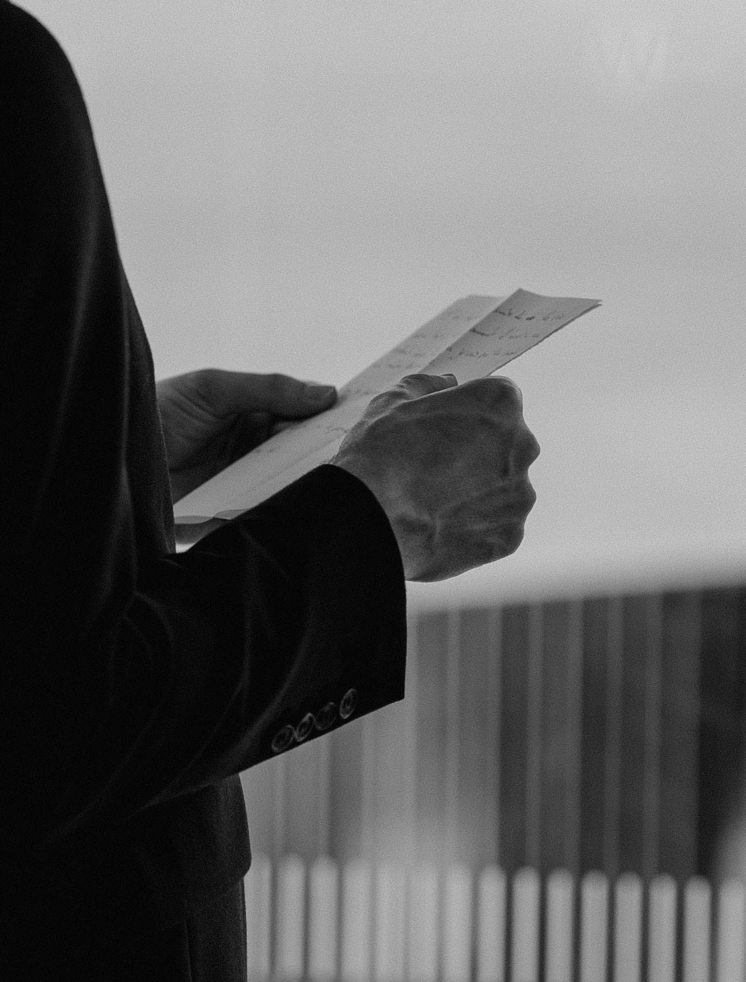 Black and white detail shot of hands holding paper during a wedding ceremony.