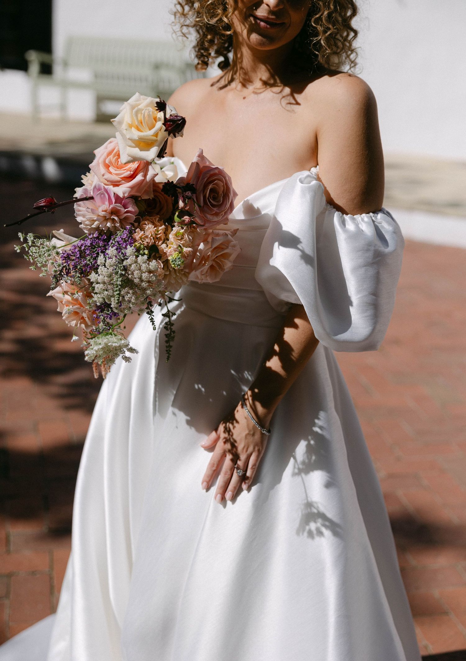 Bridal bouquet with peach roses and dried flowers complements an off-shoulder white wedding dress.