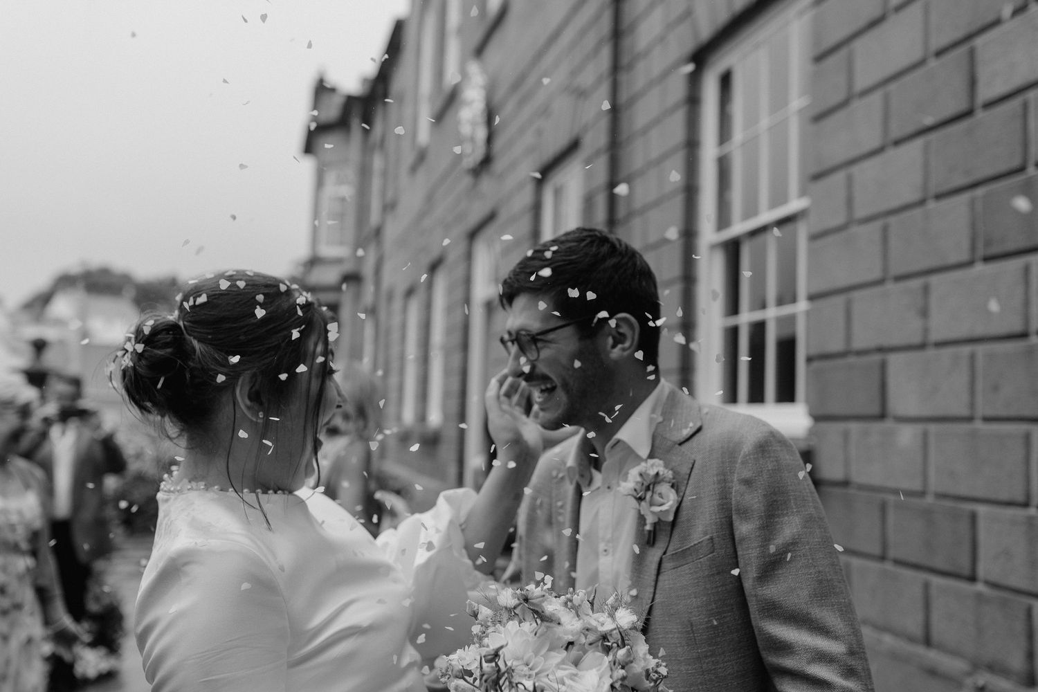Confetti falls in front of a brick building creating a festive wedding celebration atmosphere.