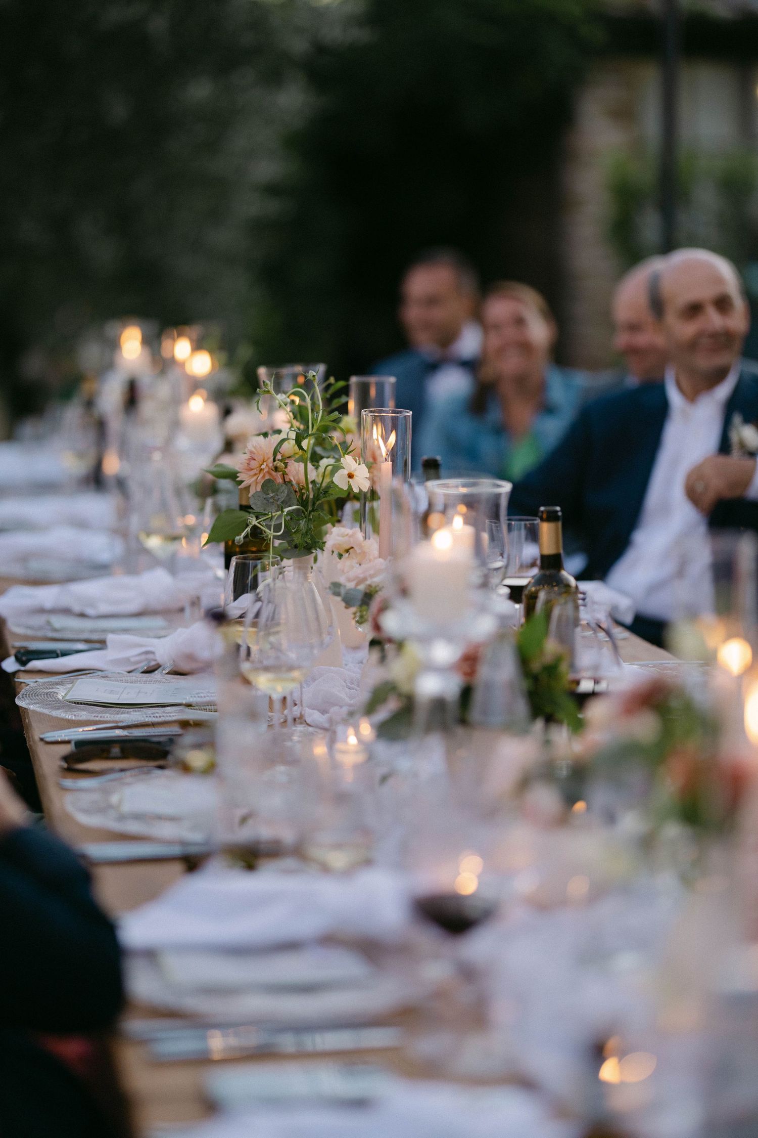 An elegant outdoor wedding reception table set with candles and floral centerpieces at dusk.