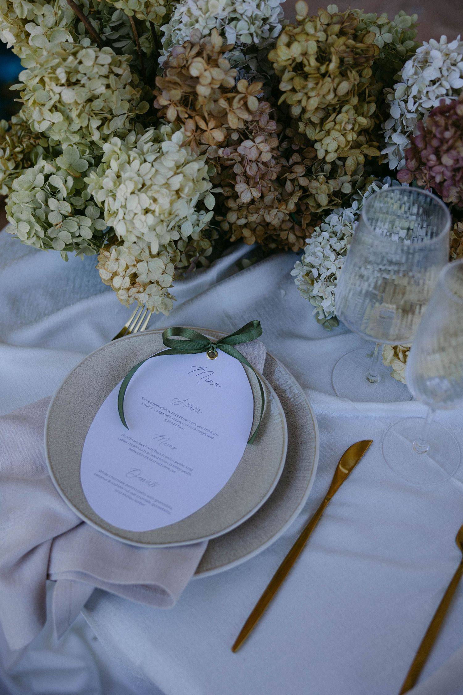 Elegant table setting with white hydrangea centerpieces and place settings on crisp white linens.