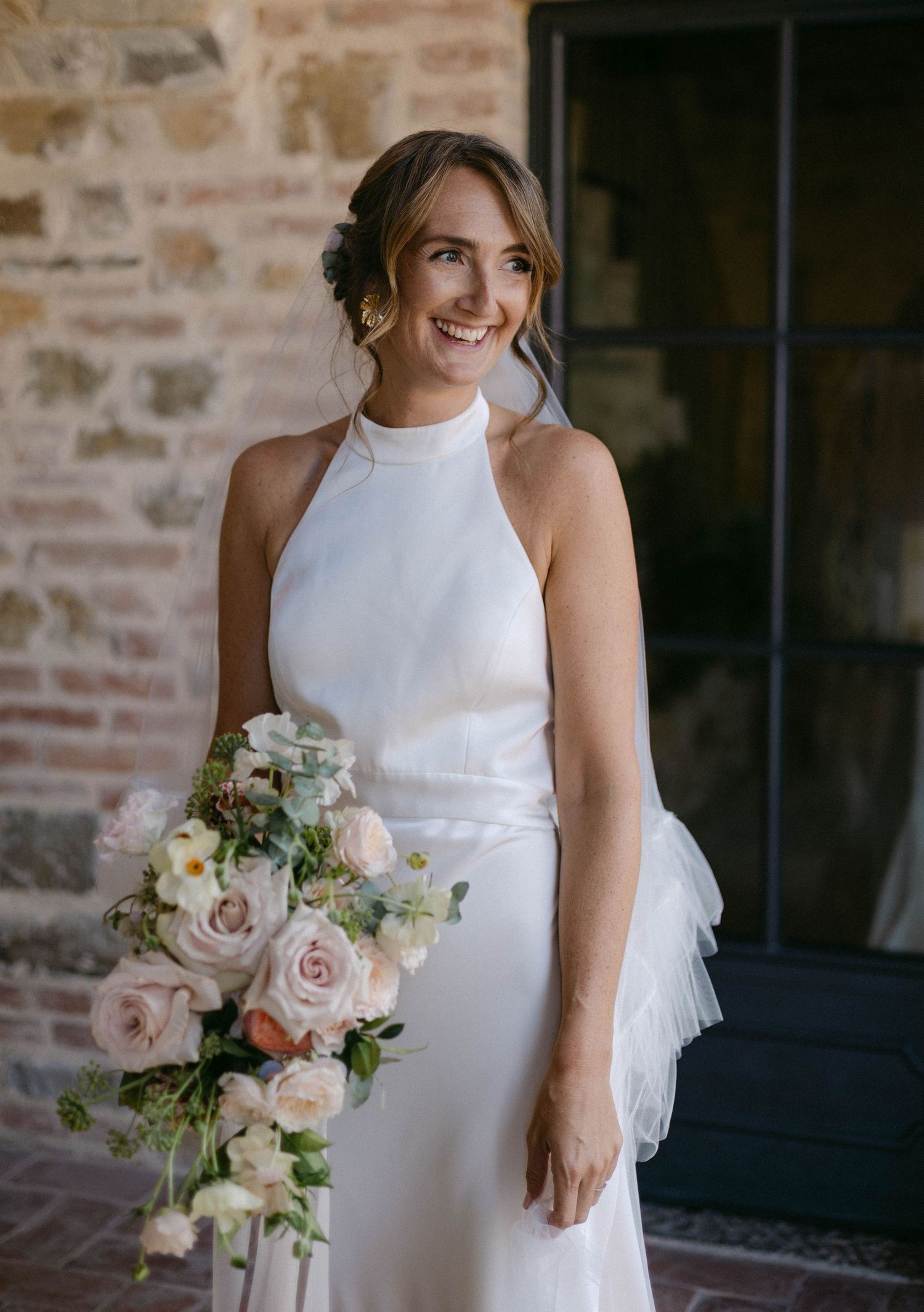 Elegant bride in a sleek white high-neck wedding dress holding a soft pink and white bouquet.